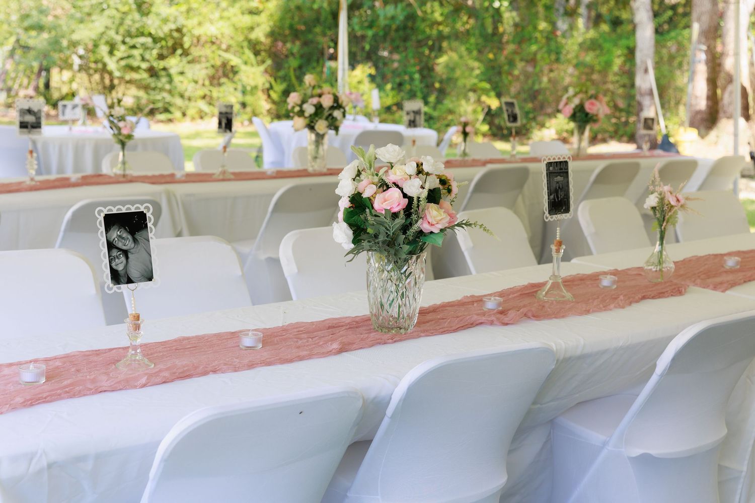 Long banquet tables with white linens and chairs are decorated with floral centerpieces for an elegant wedding reception.