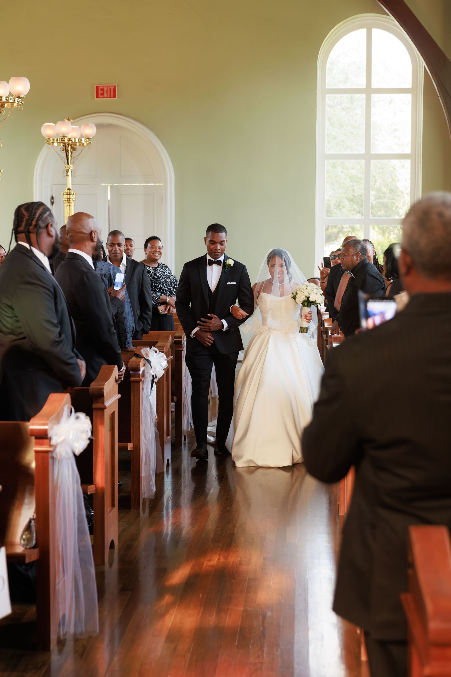 Wedding party stands in a traditional church setting with wooden pews and warm lighting during ceremony.