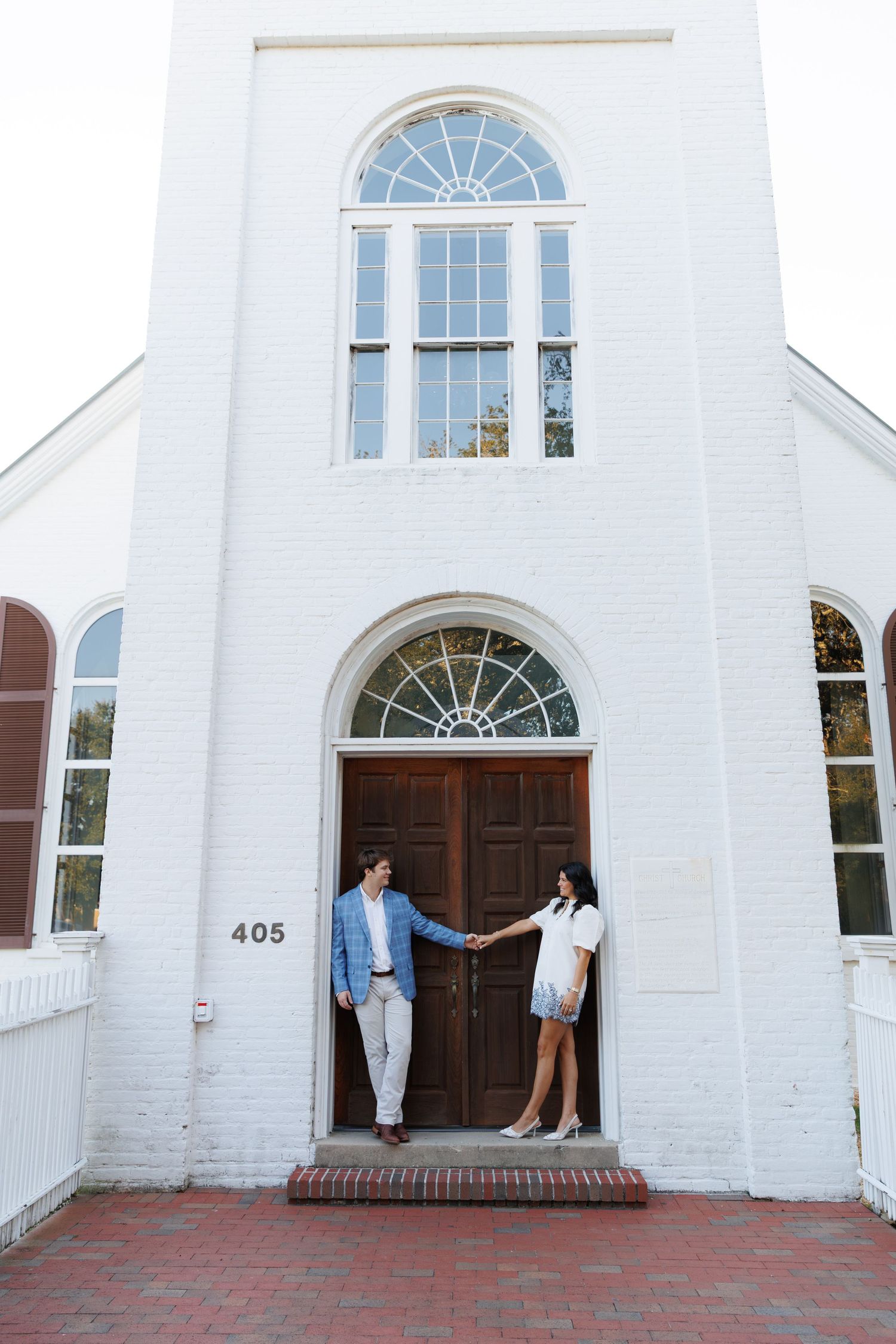 A series of white church doorways with arched windows and red brick steps leading to wooden doors.