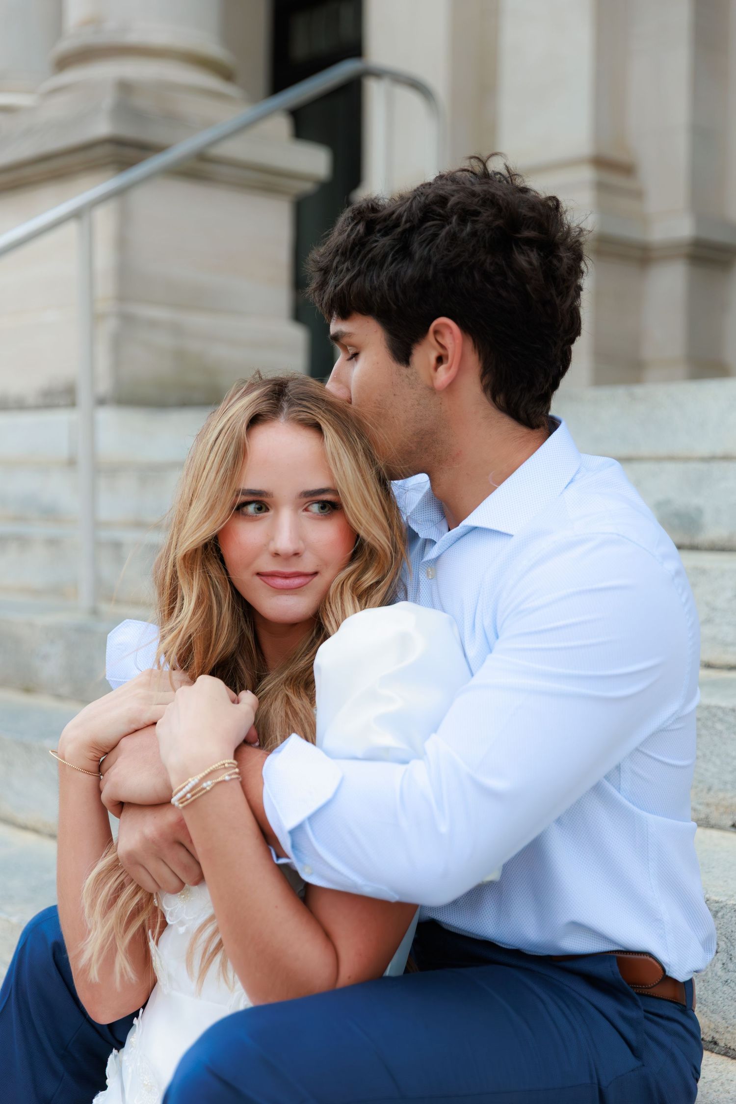 A romantic couple shares intimate moments while sitting on the steps of a classical building.