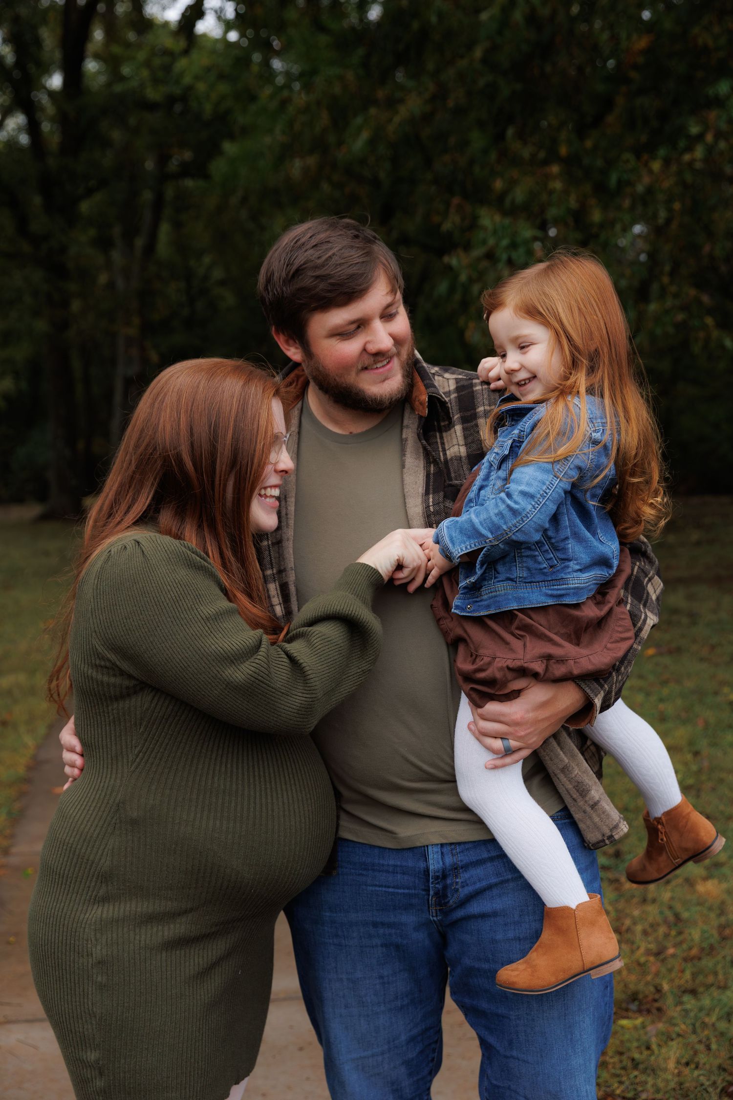 A family shares a joyful moment together outdoors during autumn, with the parent wearing olive green and holding a small child.