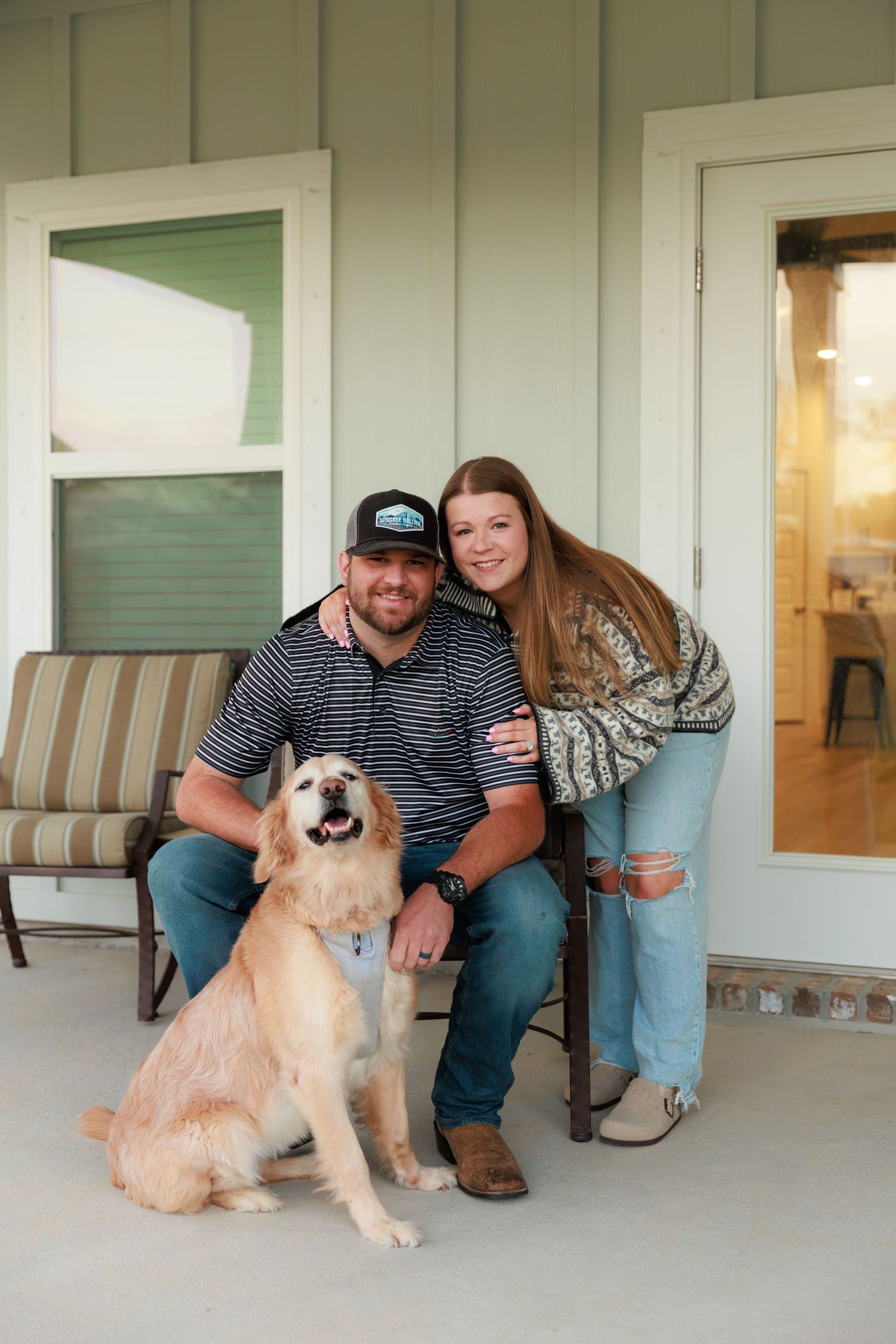 A happy golden retriever poses with people on a front porch with striped cushioned bench seating.