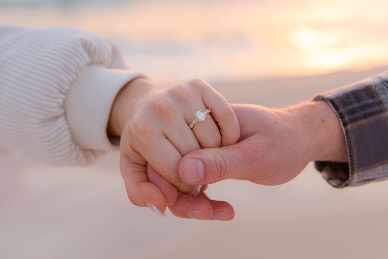 Two hands reach towards each other against a warm sunset sky in a romantic gesture.