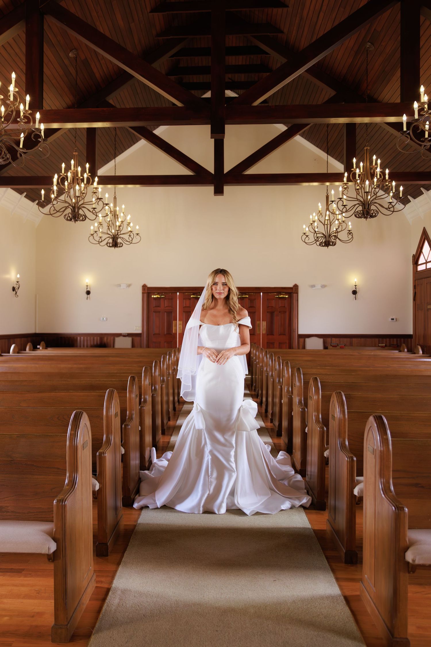 Elegant wedding chapel interior with wooden pews, exposed beam ceiling, and crystal chandeliers creates romantic ambiance.