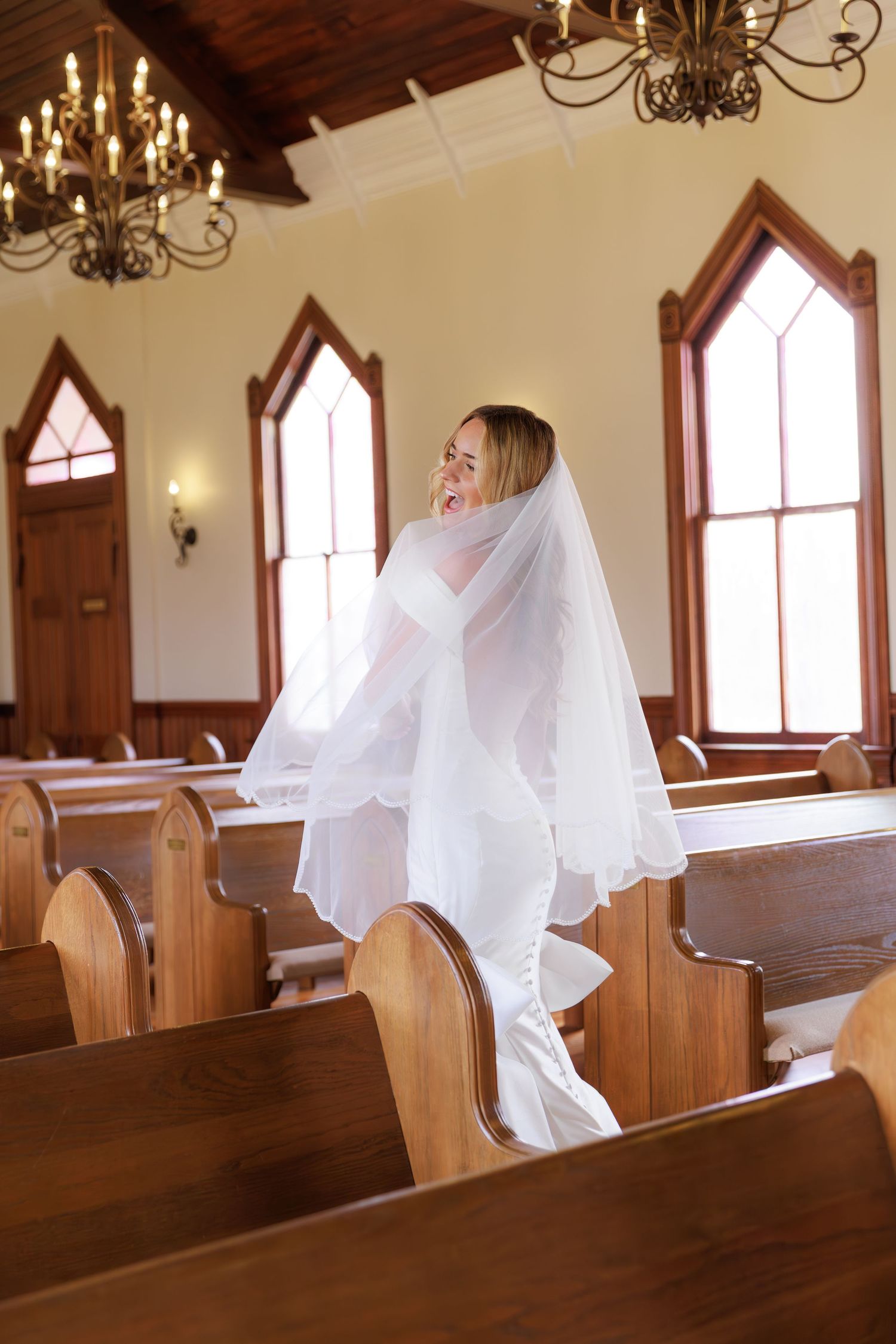 A sequence of four photos showing a figure in white flowing fabric moving through wooden church pews beneath chandeliers.