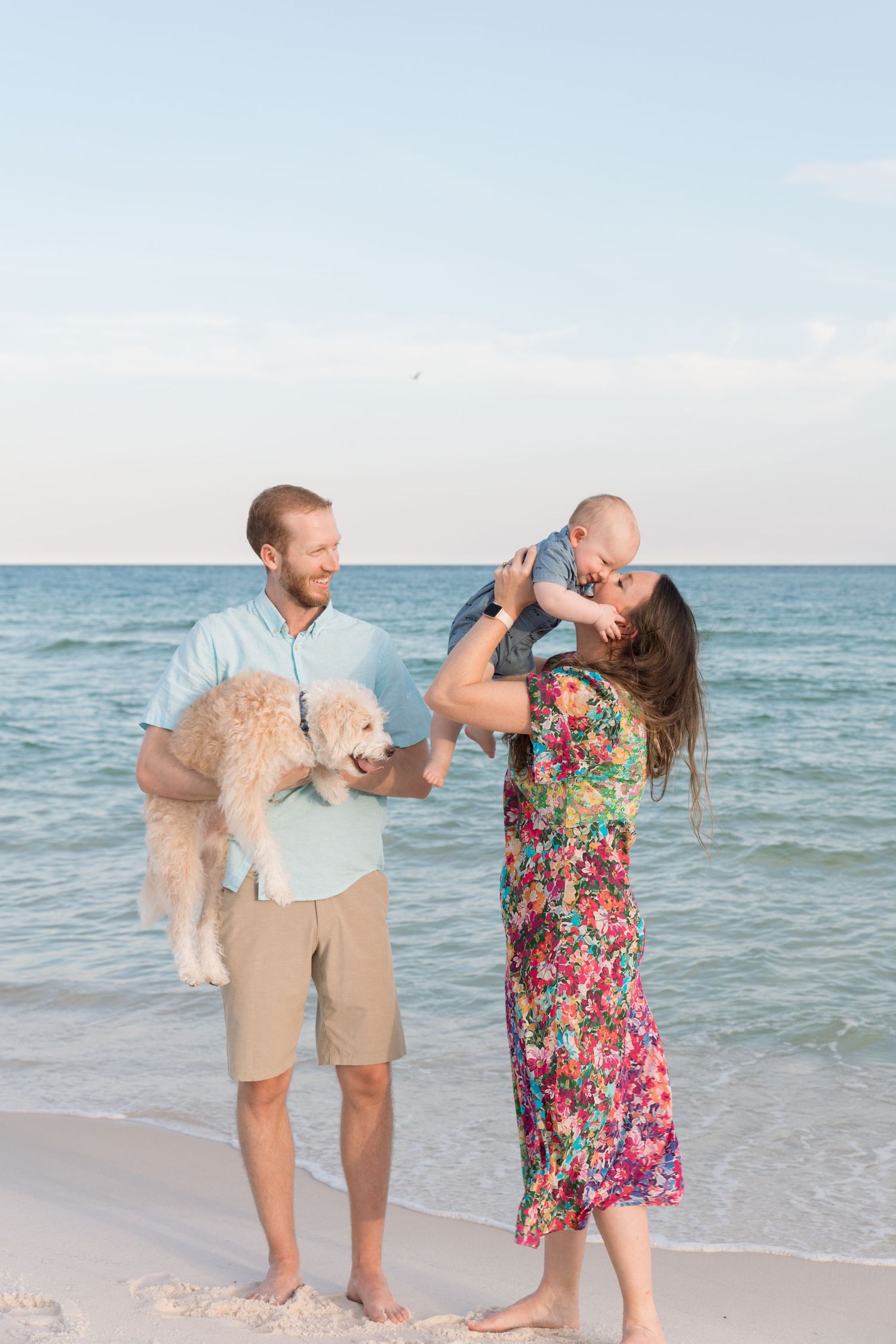 A couple and their fluffy white dog share playful moments together on a sunny beach by the ocean.