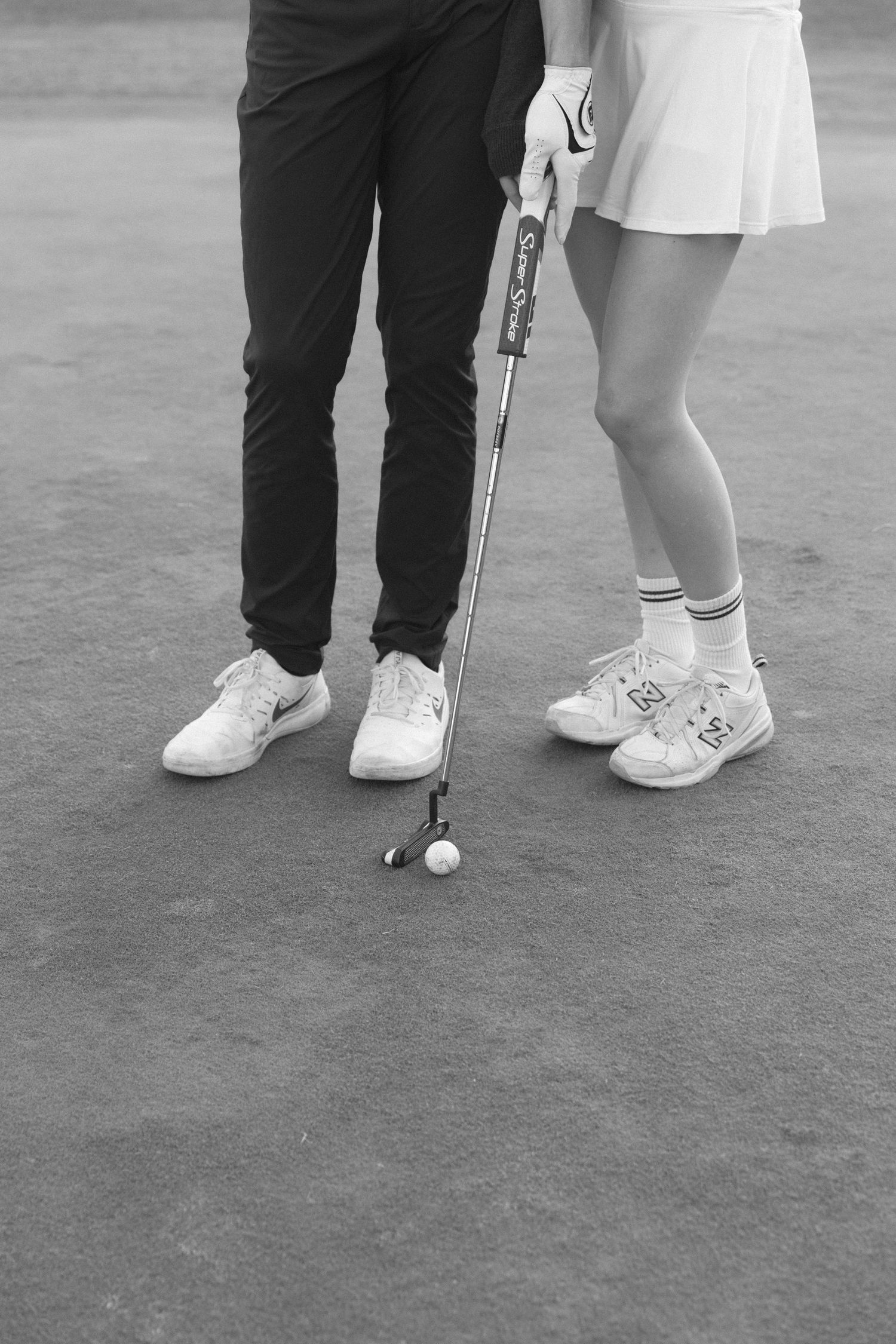 Black and white photo showing feet in contrasting outfits - one in dark pants and the other in a white dress.