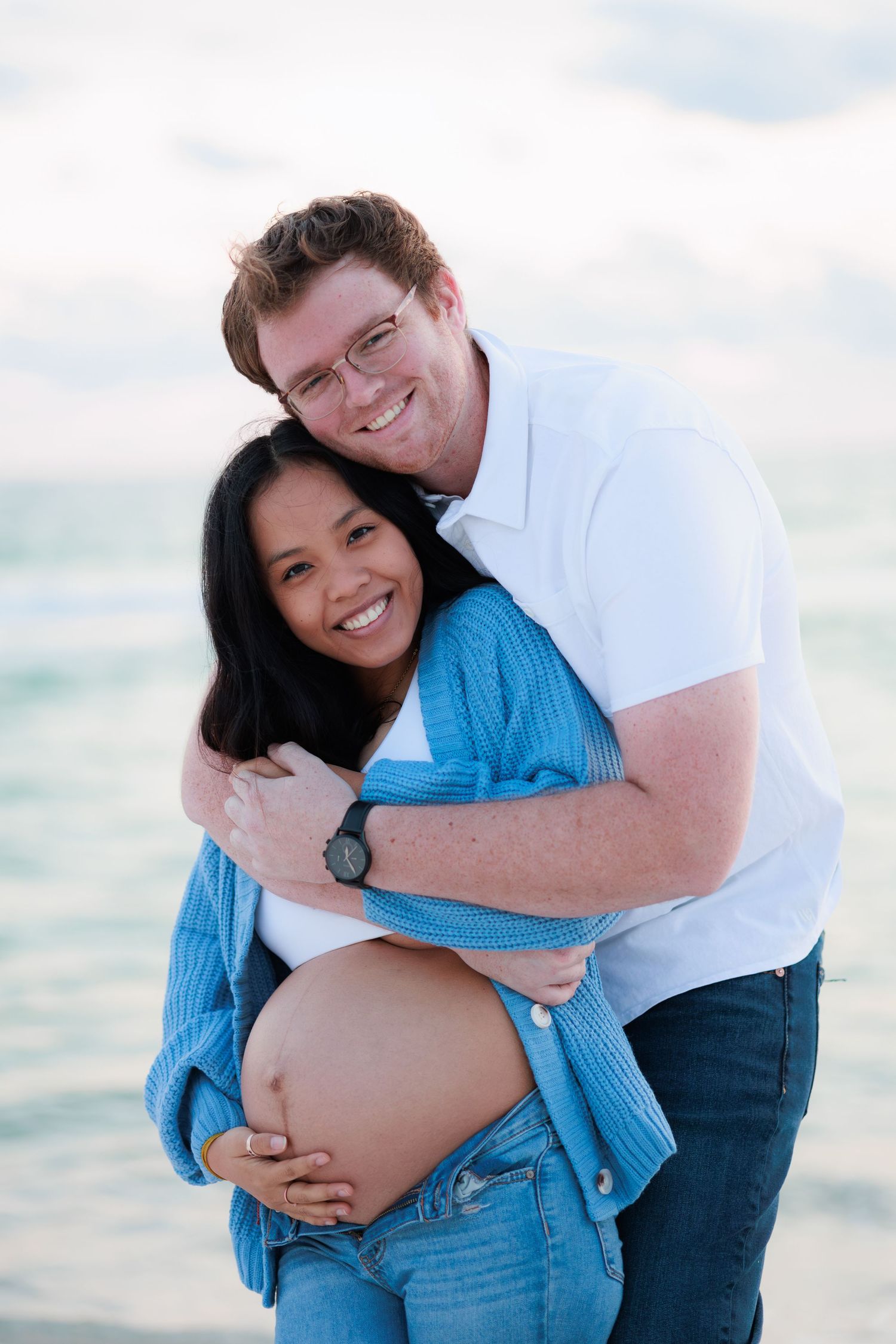 Sweet candid moments of an expecting couple embracing on the beach during their maternity photoshoot.