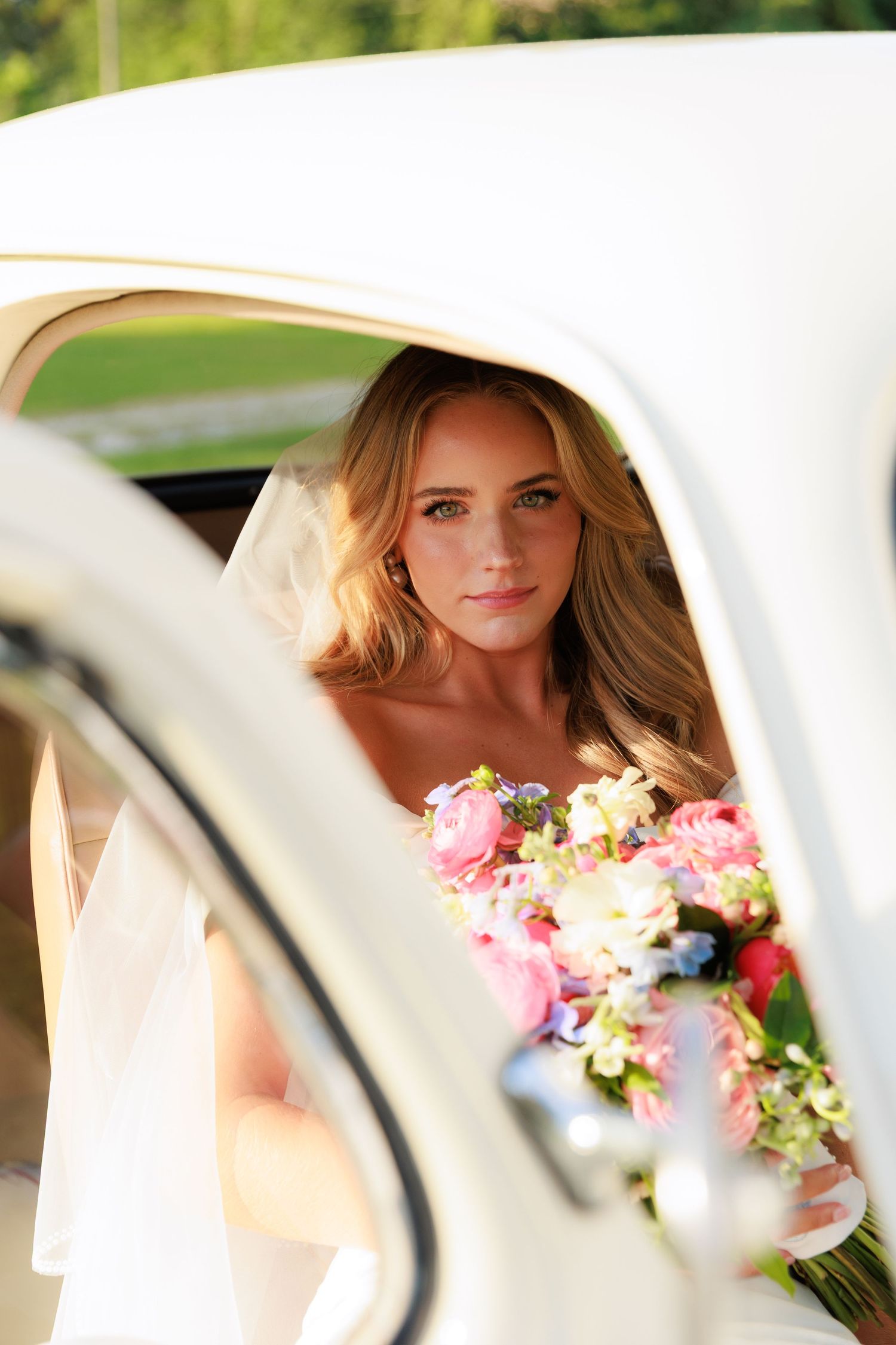Classic white wedding car with bridal bouquet of pink and blue flowers.