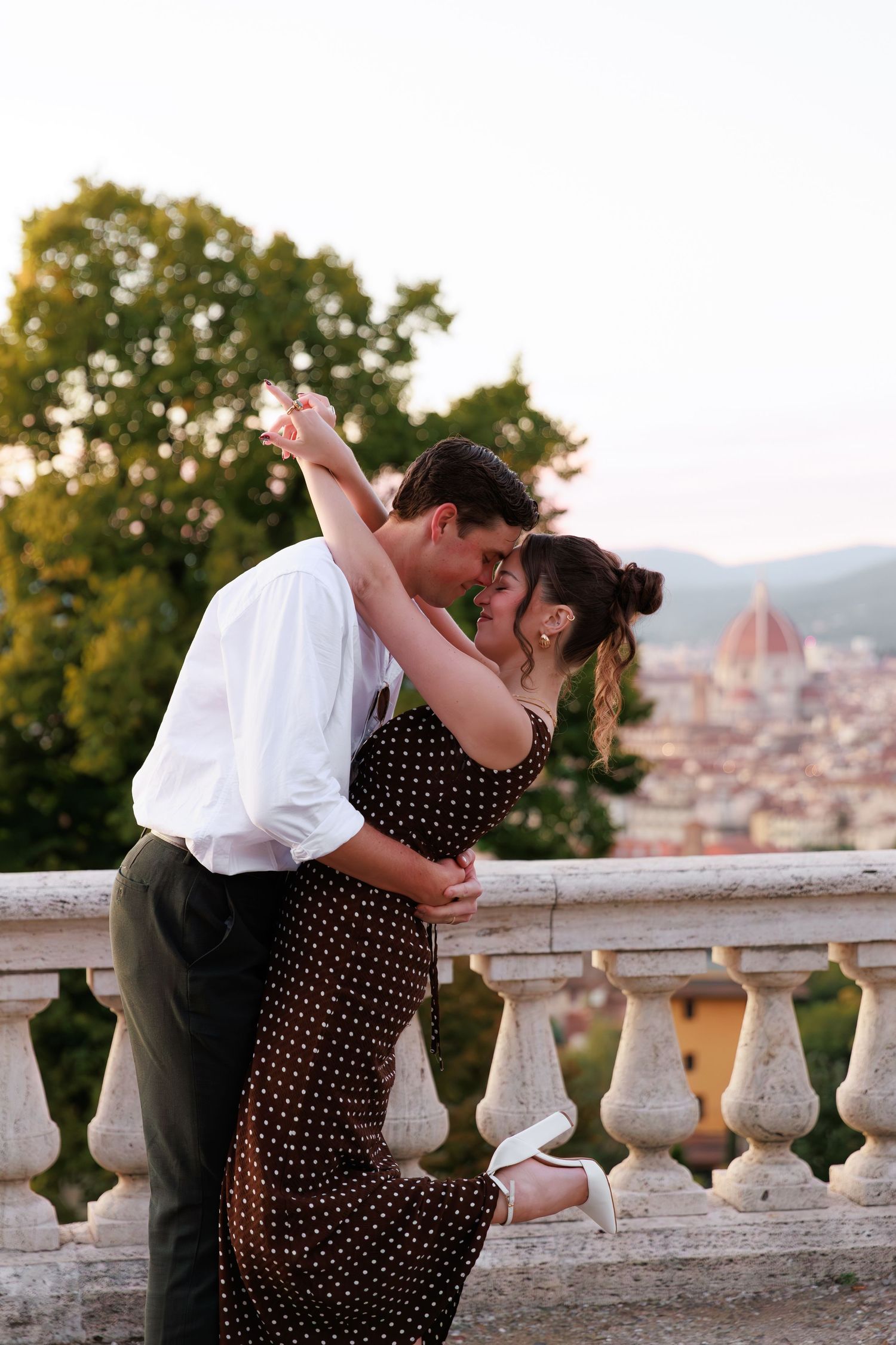 Couple sharing romantic dip kiss on terrace with Florence cathedral dome in background at sunset.