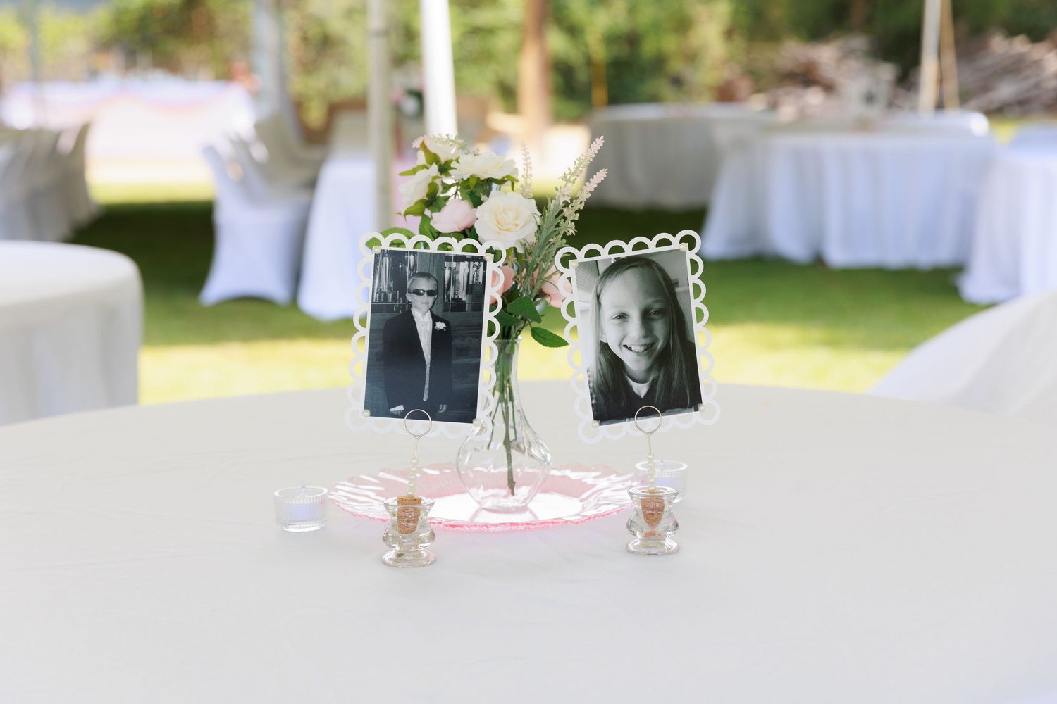 Elegant outdoor wedding reception setup with white tables, chairs and floral arrangements in a garden setting.