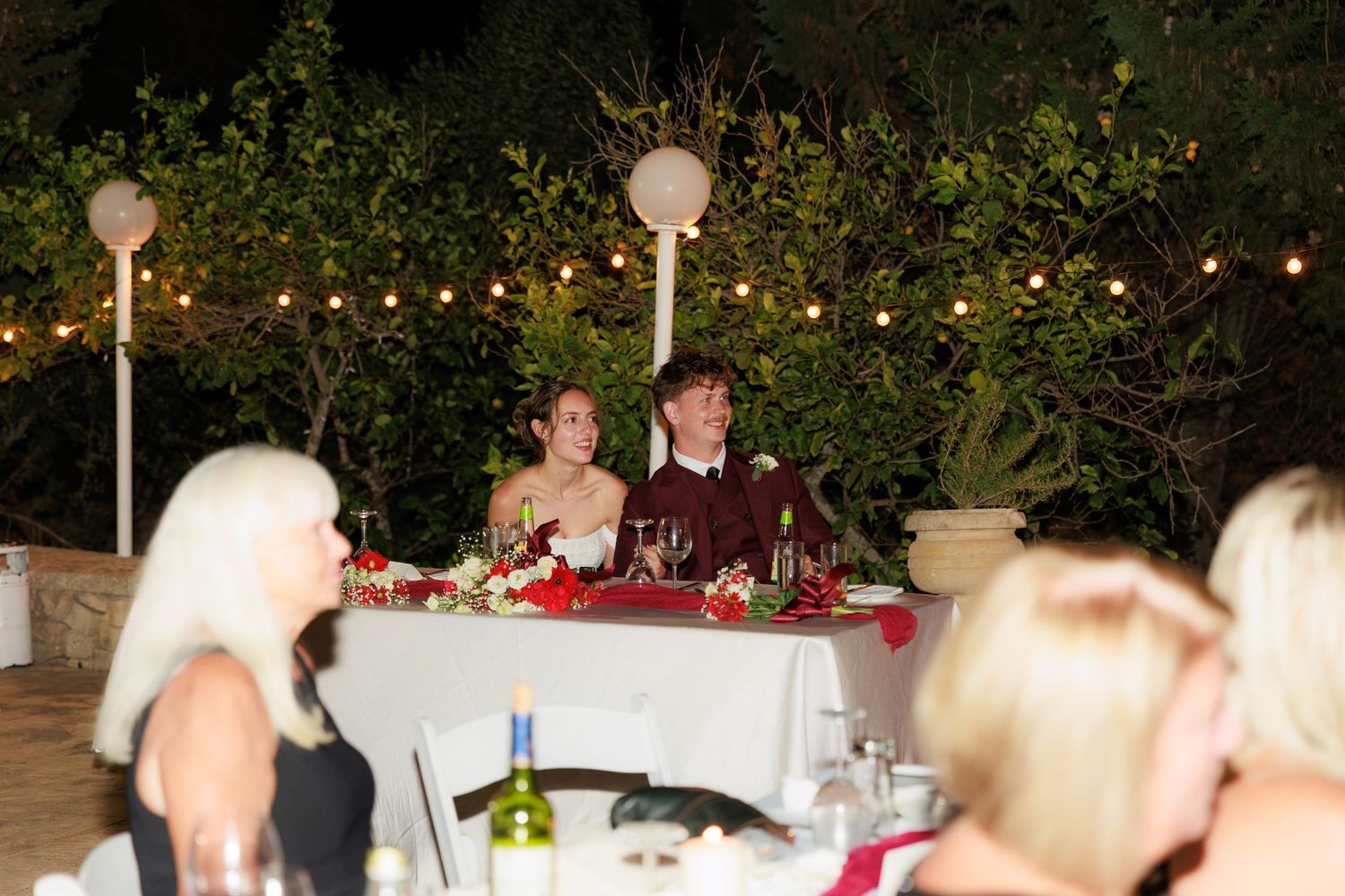 People enjoying an outdoor evening dinner party under string lights with long tables set up in a garden setting.