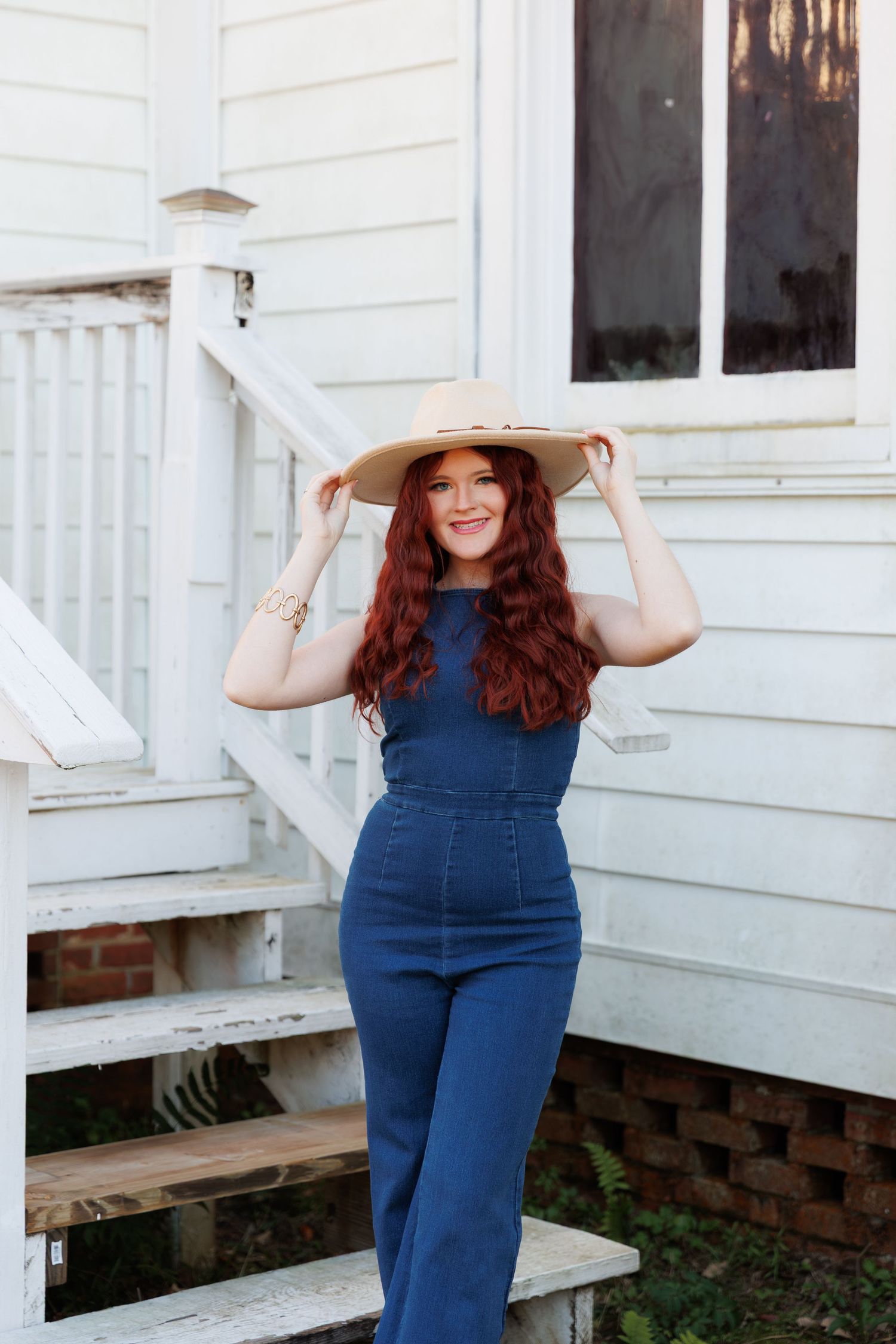 Woman in denim jumpsuit smiles while posing on white porch steps.