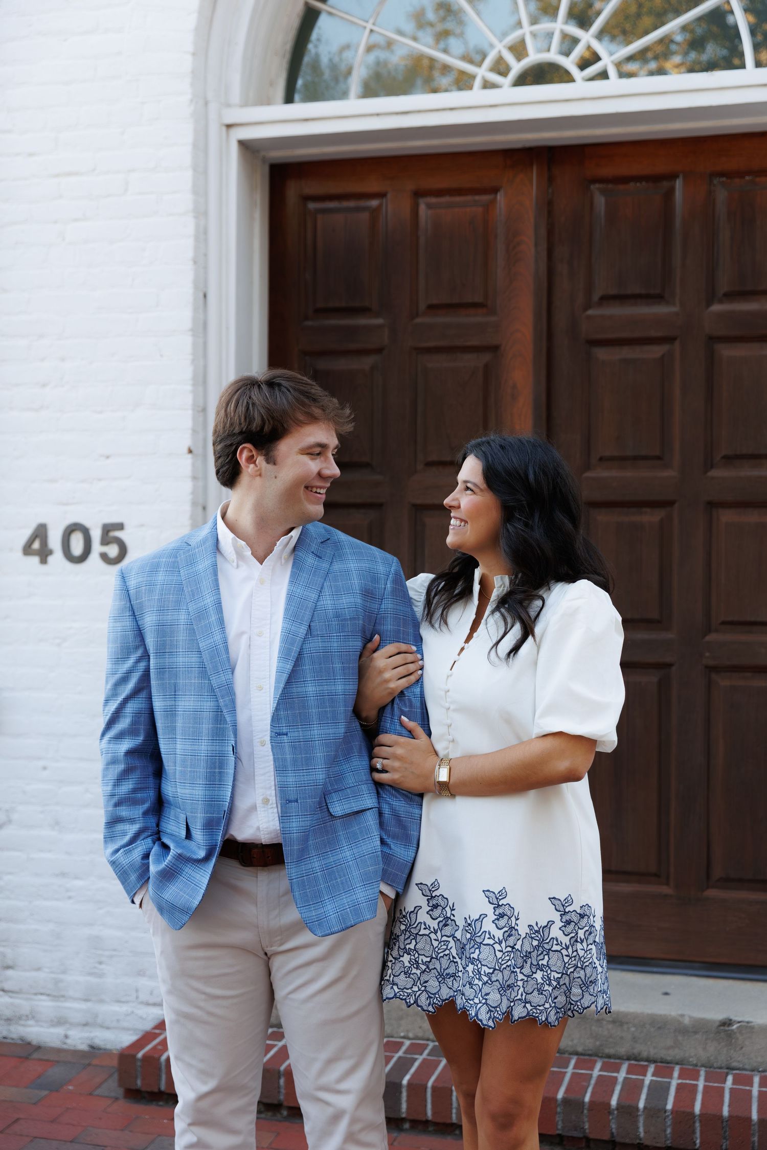 A couple shares a candid moment together while wearing coordinated blue and white outfits against a white brick wall.
