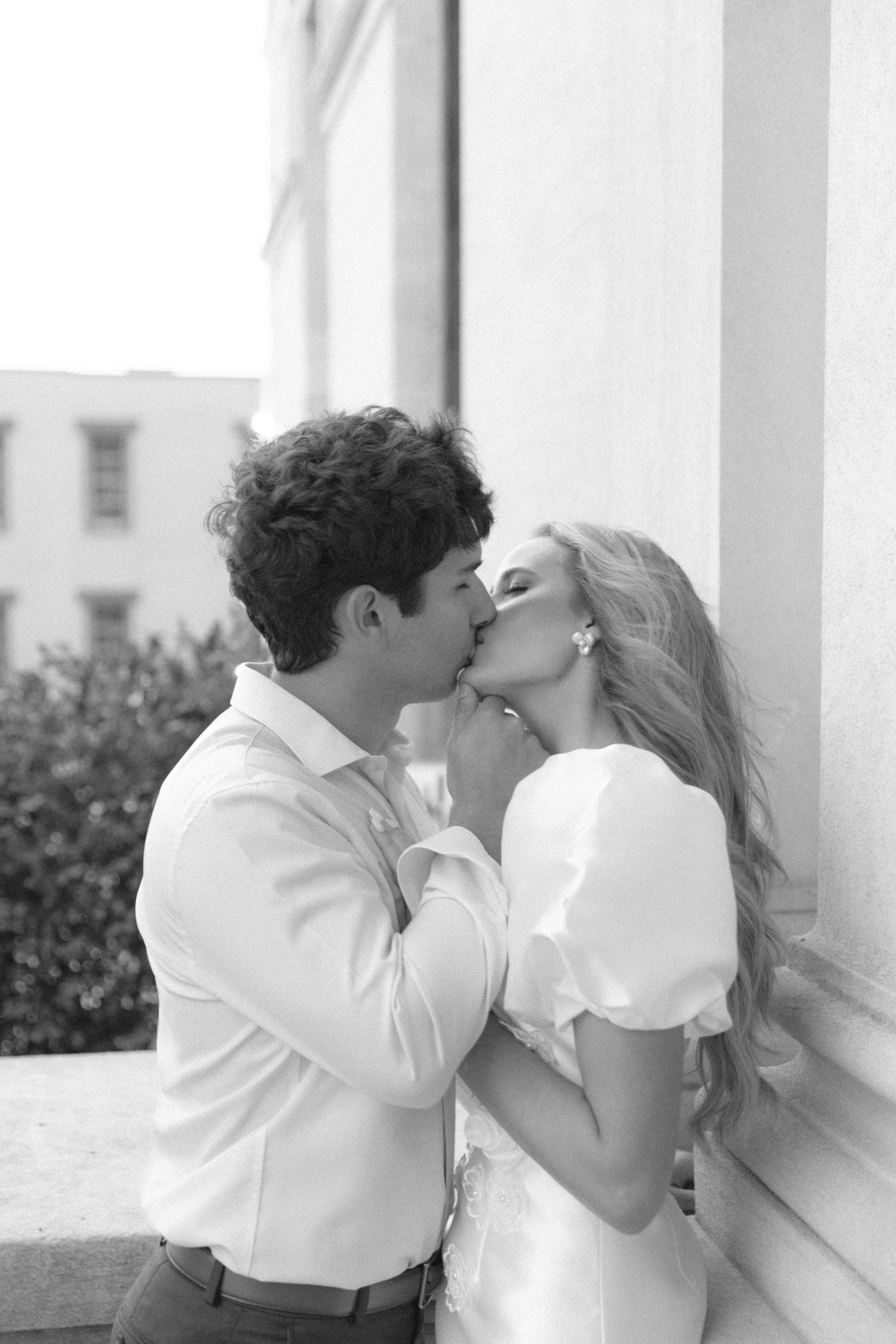 A romantic black and white portrait of a couple sharing an intimate moment against a white wall.