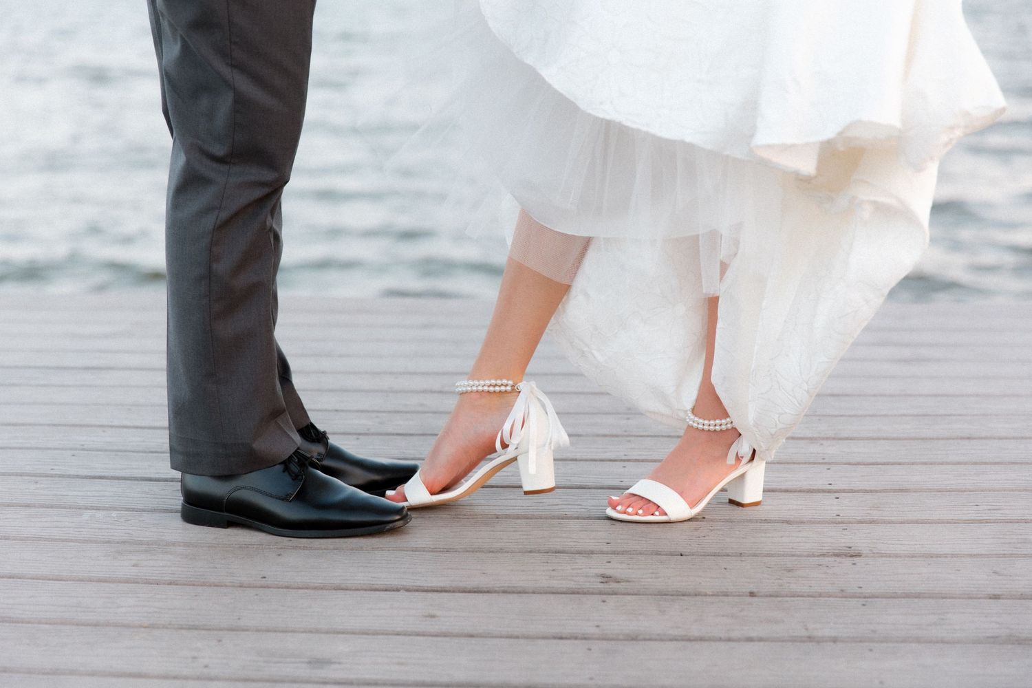 Close-up of wedding shoes and dress hem on wooden dock.