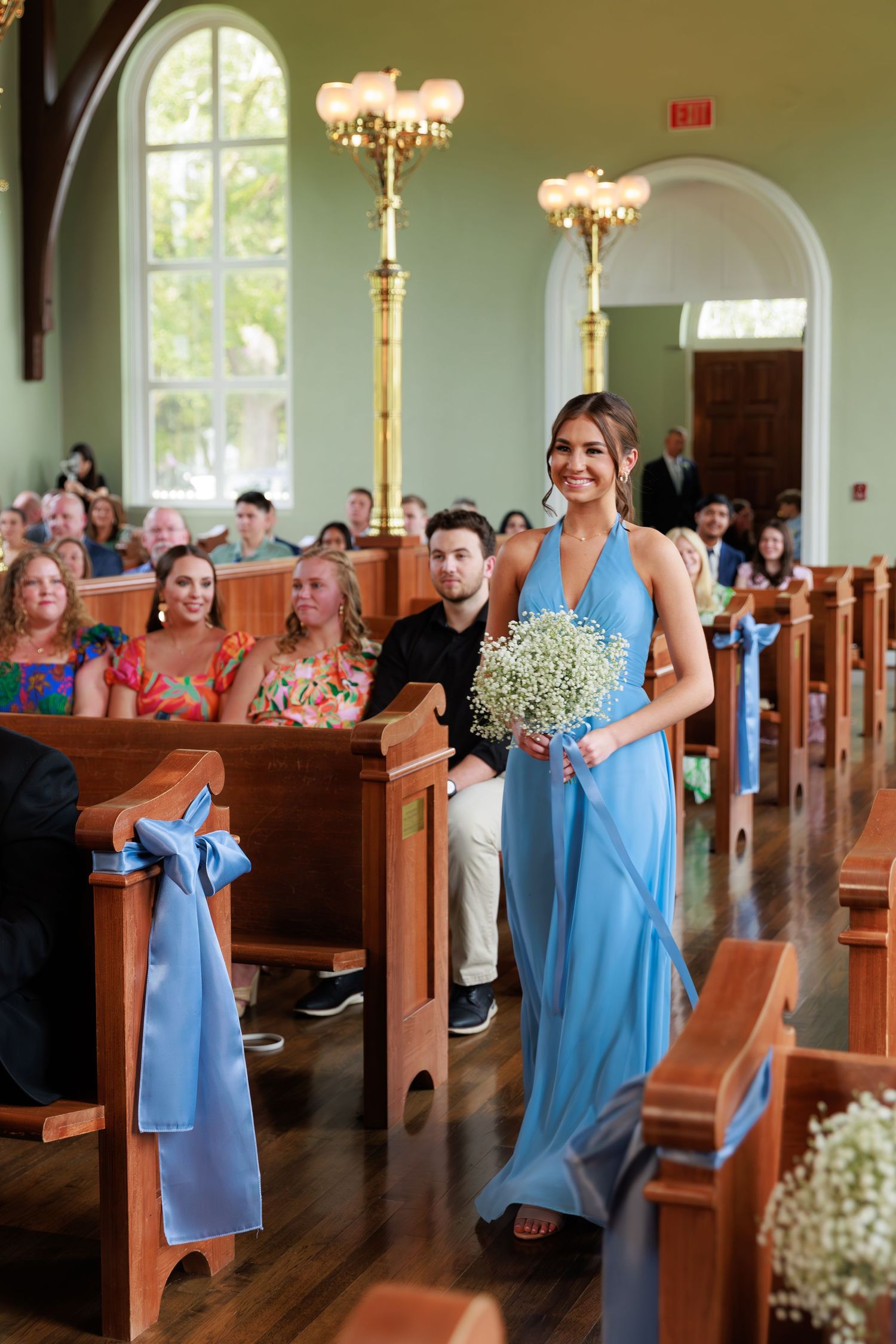 Wedding processional with bridesmaids in blue dresses walking down church aisle.