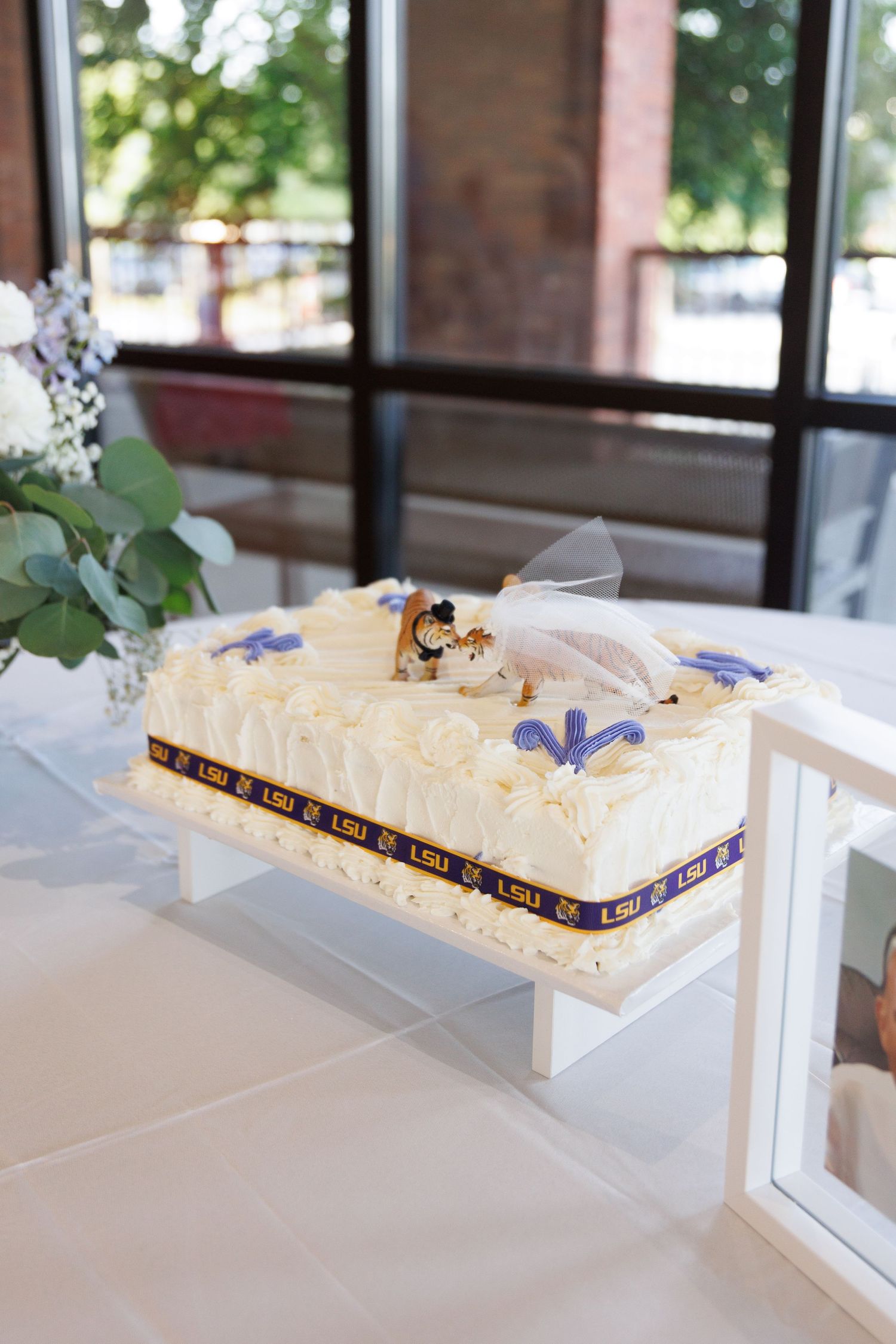 White wedding cake decorated with purple flowers and ribbon on display at reception.