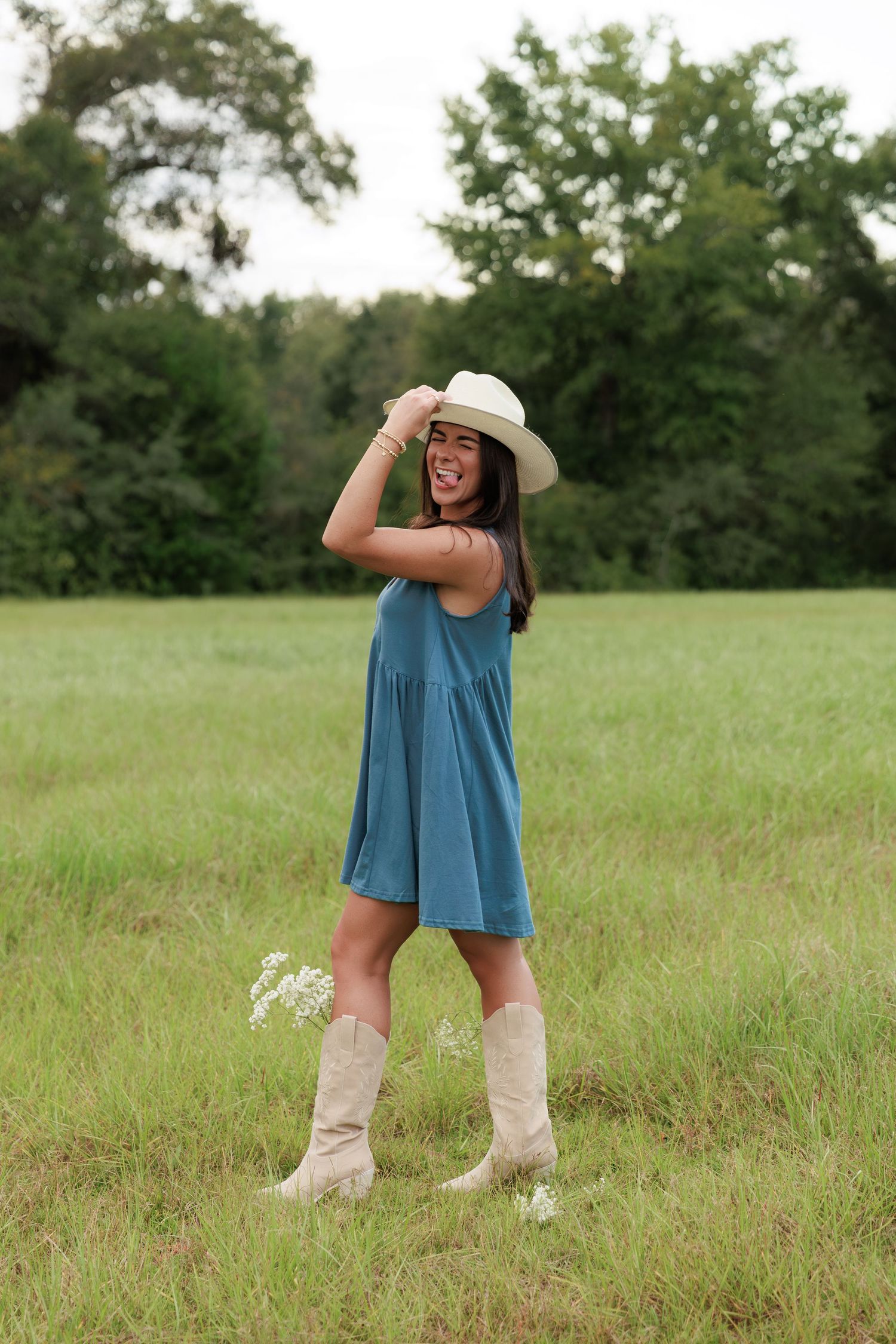 Joyful outdoor portrait showcasing western style with boots and a white hat against green trees.