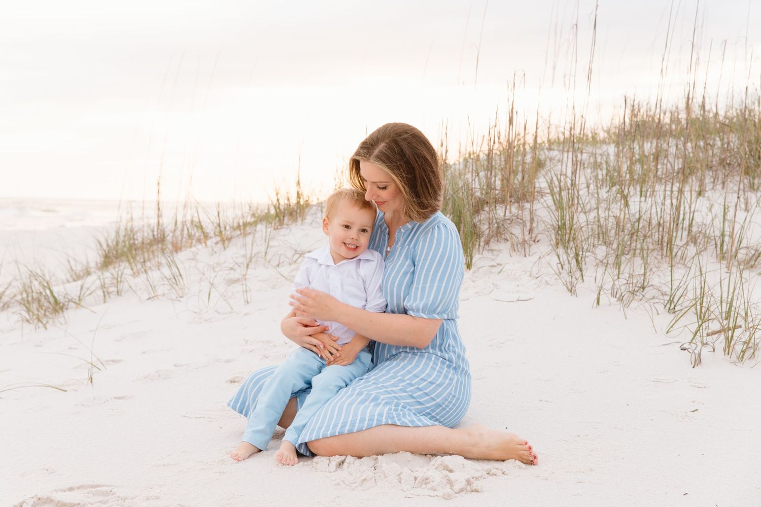Mother and baby share tender moment on white sand beach at sunset.