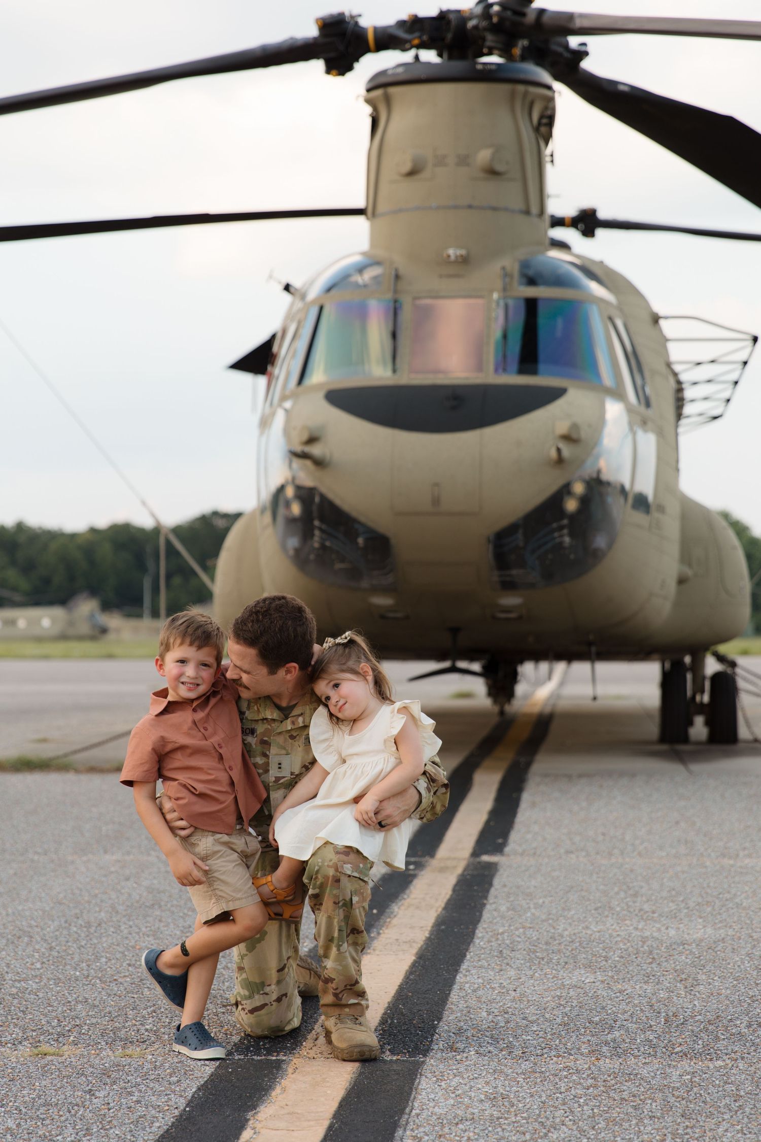 Service member with children posing in front of Chinook helicopter.