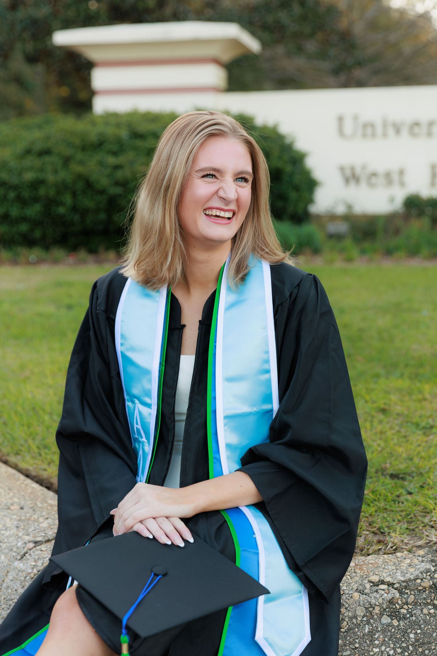 Graduate in black cap and gown with light blue stole poses outdoors during graduation photoshoot.