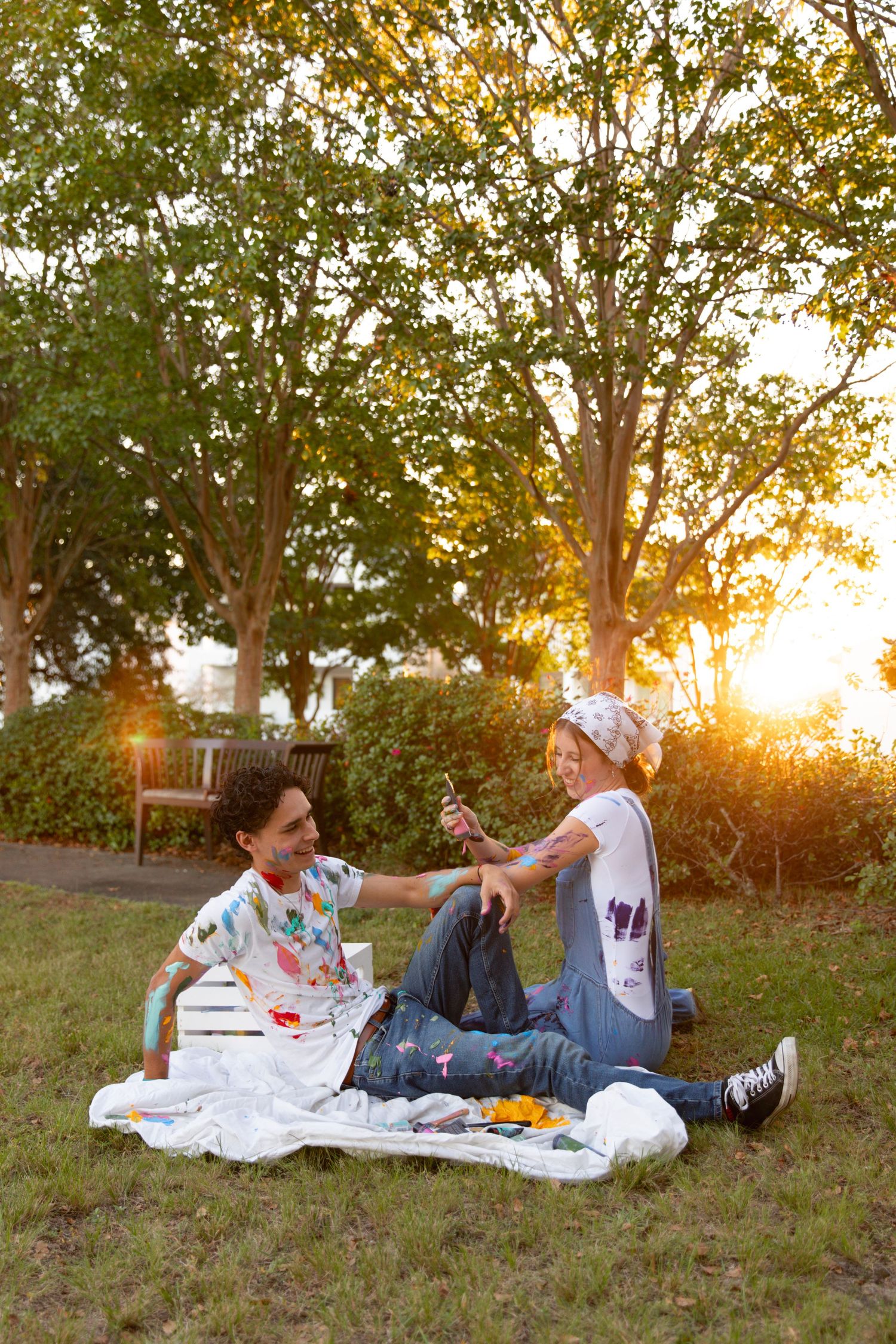 A couple relaxes on a blanket during sunset in a grassy area with trees in the background.