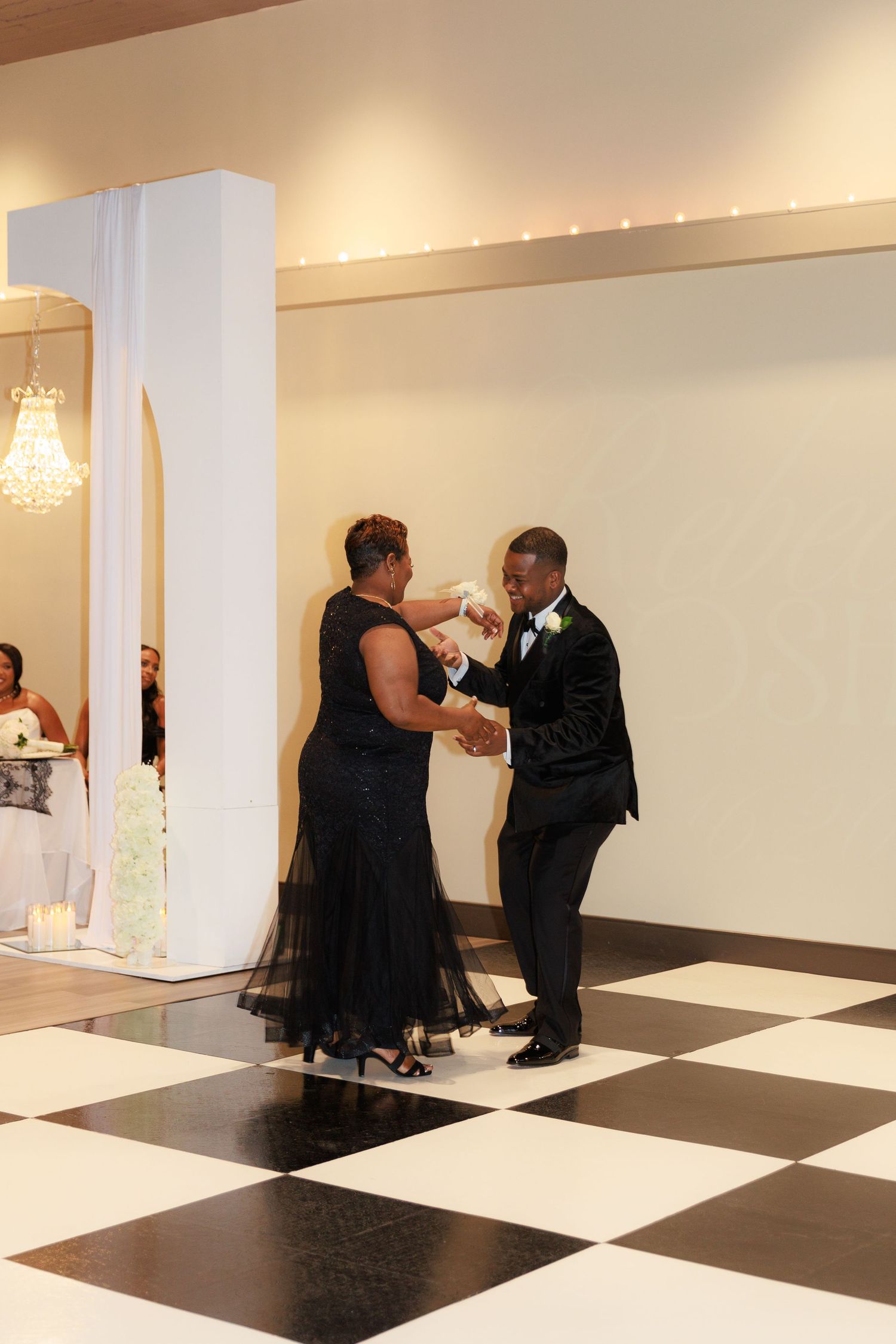 A couple shares a romantic dance on a black and white checkered ballroom floor at an elegant event venue.