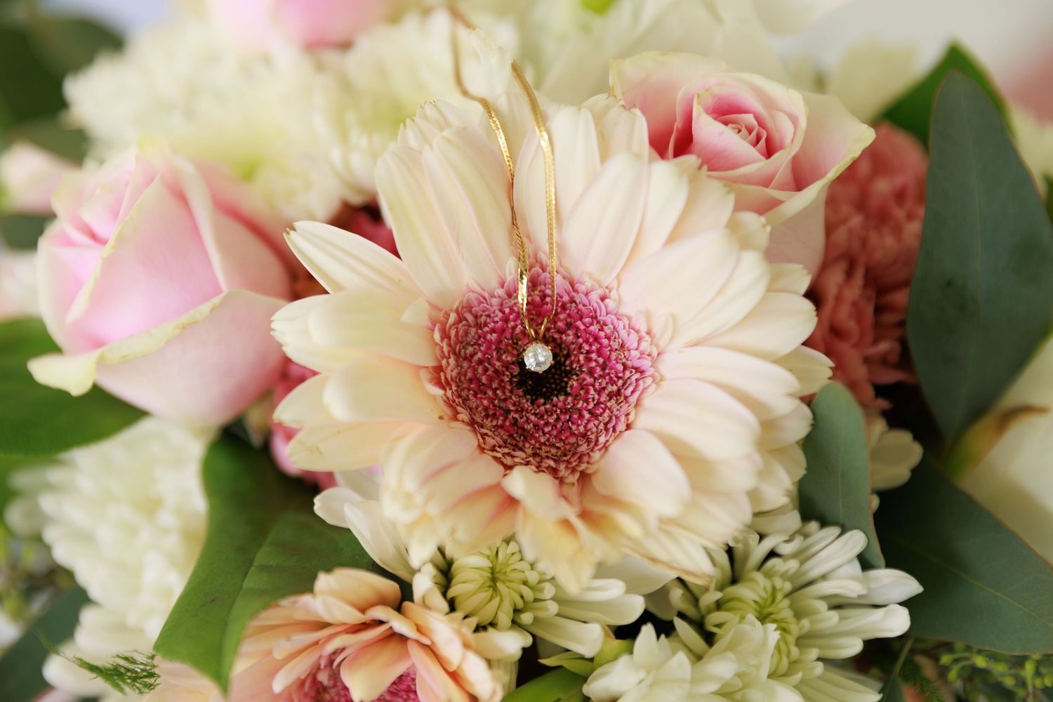 Pink and cream gerbera daisies with roses create a romantic floral arrangement with delicate green foliage.