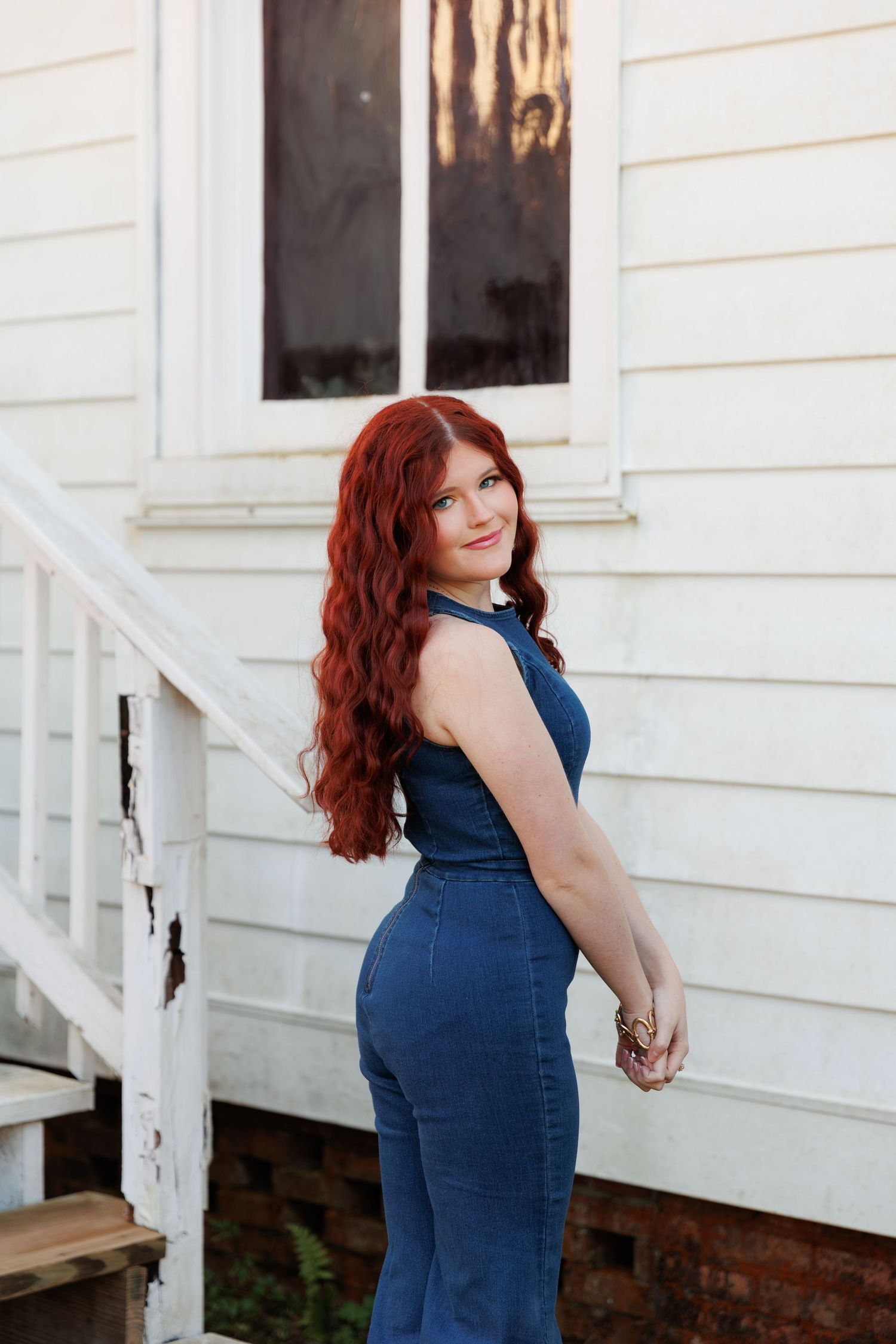 A woman with red hair poses in a navy blue dress against a white house exterior.