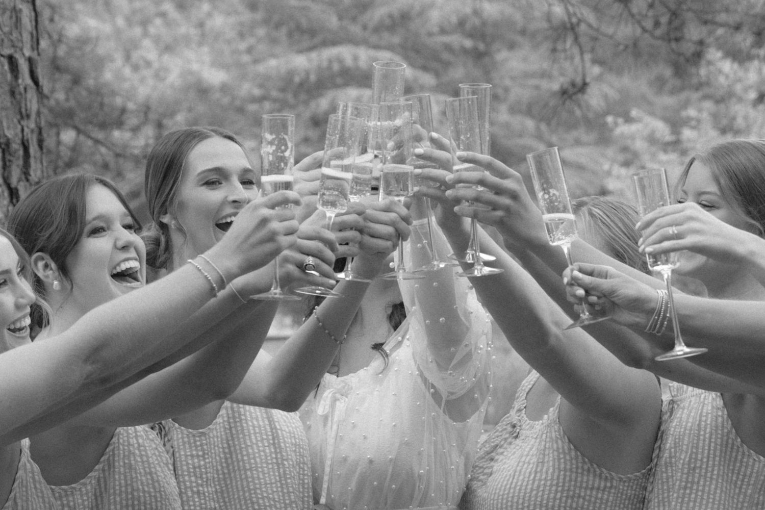 Black and white photo of bridesmaids toasting with champagne glasses at a wedding celebration.