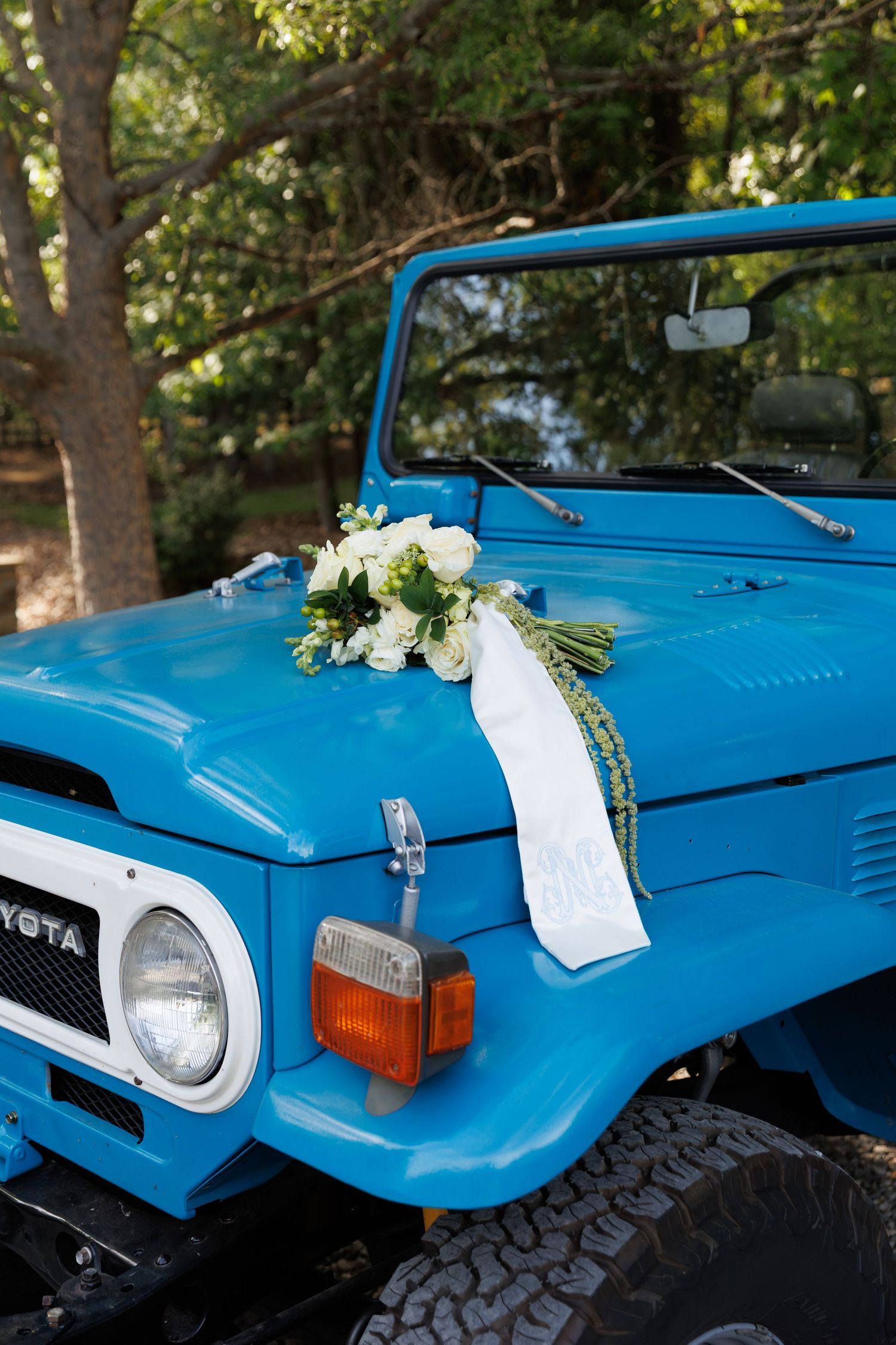 Blue vintage Toyota FJ40 Land Cruiser decorated with white floral bouquet and ribbon for a wedding ceremony.
