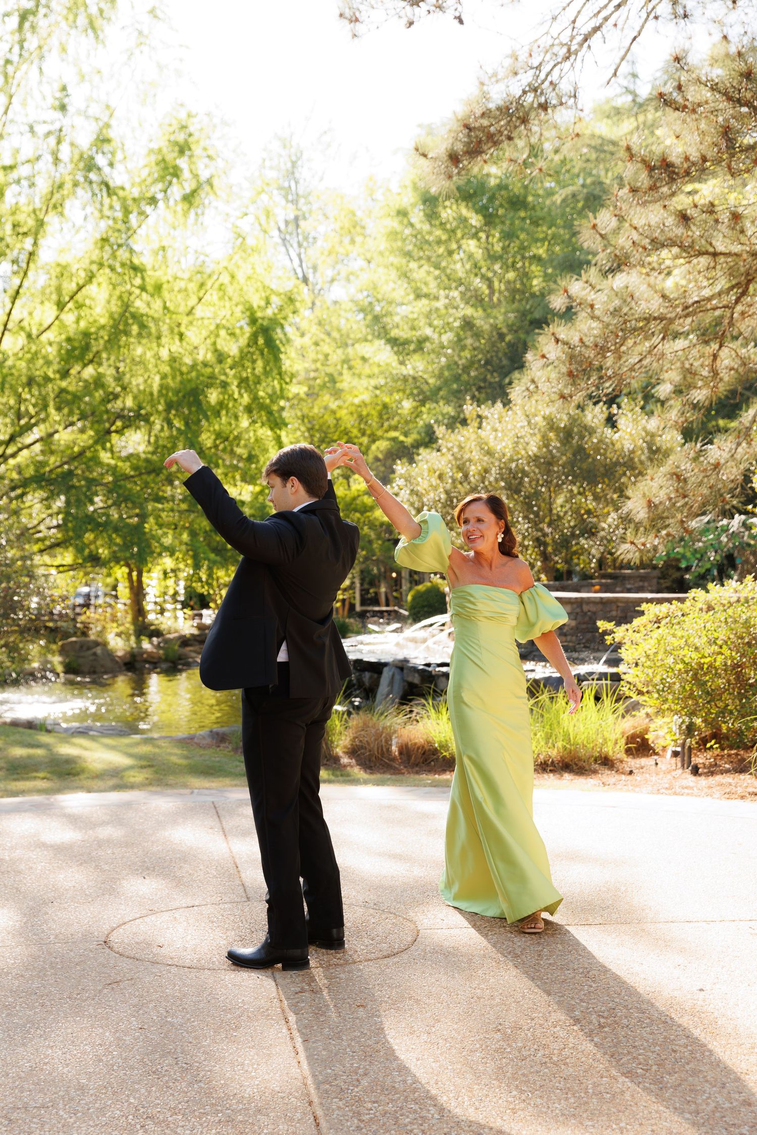 Couple dancing outdoors, woman in green off-shoulder gown being twirled by man in black suit.