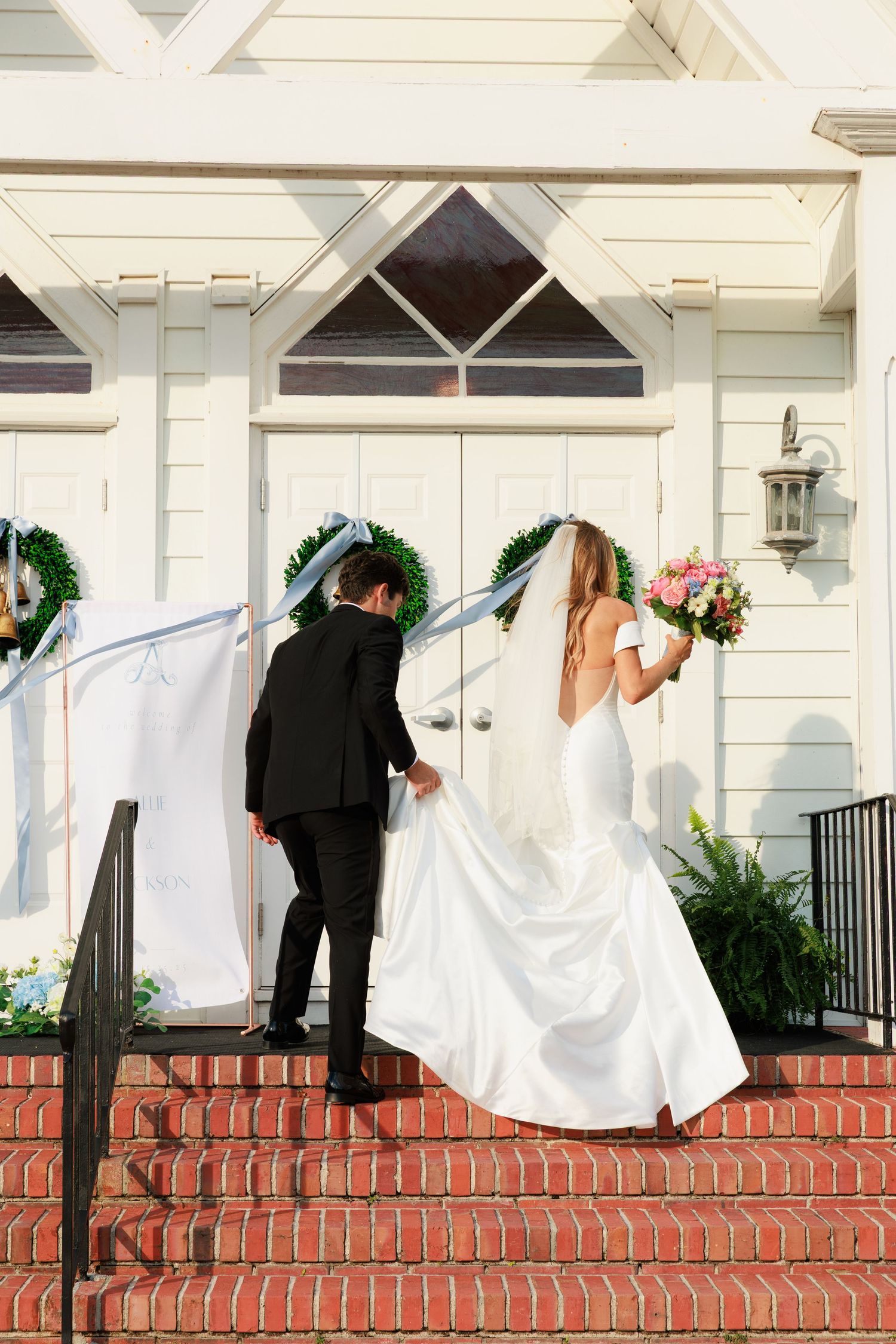 A wedding couple on red brick church steps with holiday greenery wreaths on white church exterior.