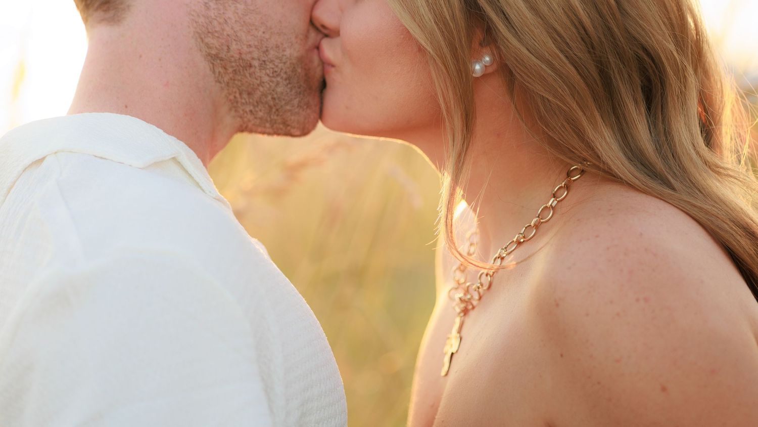 A couple embraces in a romantic golden-hour setting with soft sunlight illuminating their silhouettes.