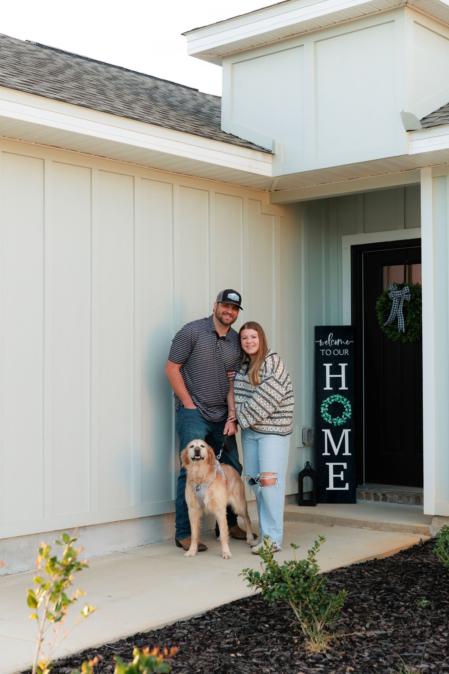 A couple stands with their golden retriever dog on the front porch of their new home.
