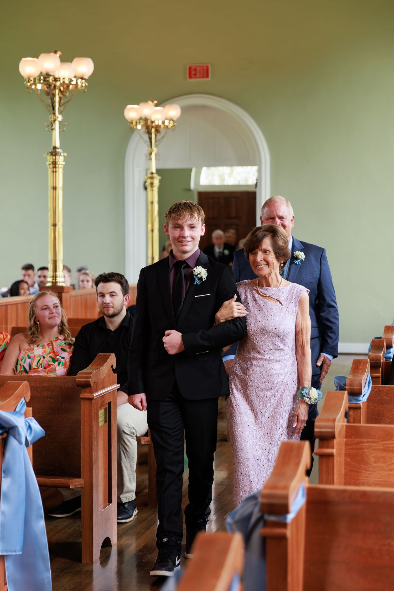 Wedding attendants in blue dresses and dark suits process down a church aisle.