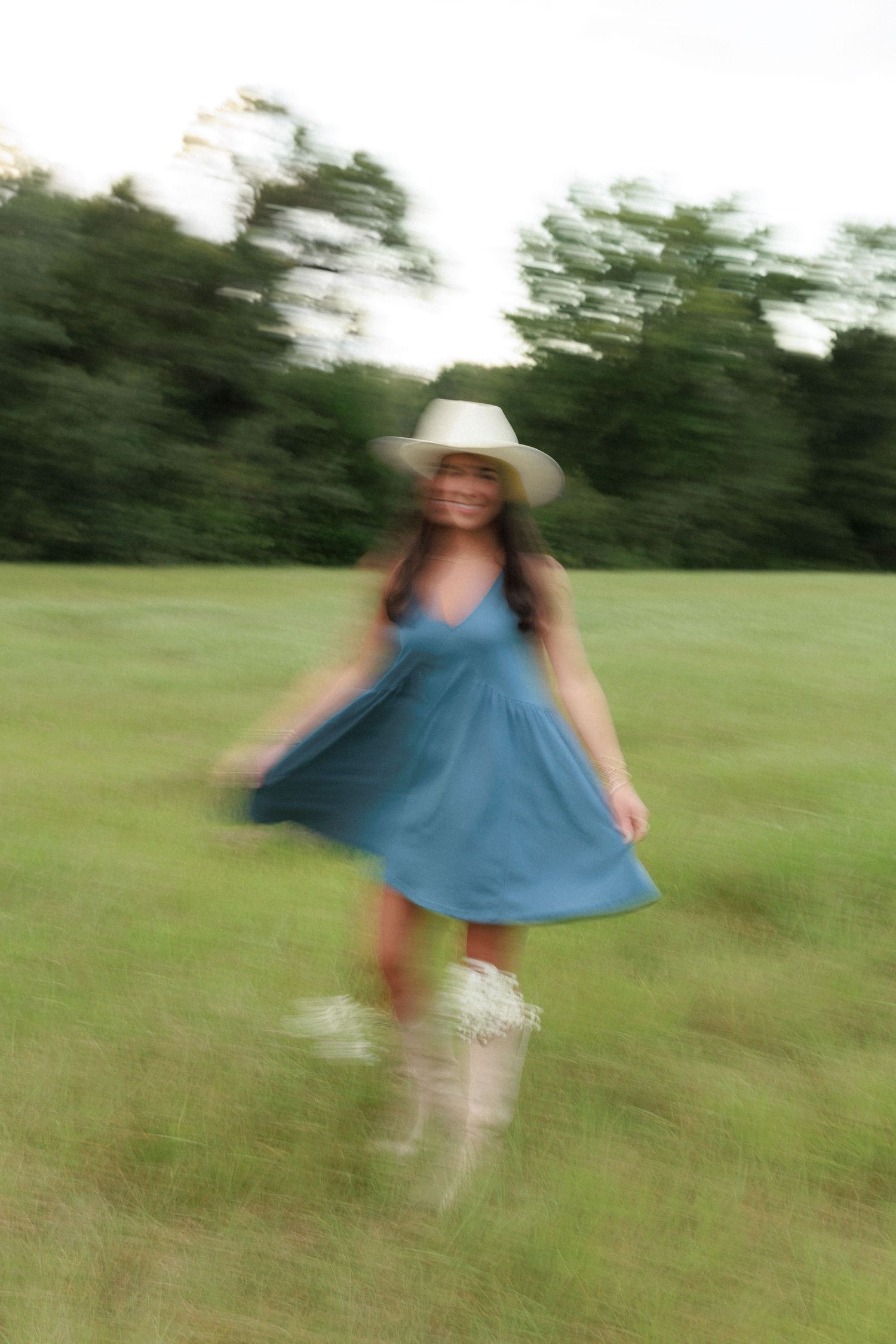 Motion-blurred photo of woman twirling in blue dress and cowboy hat.