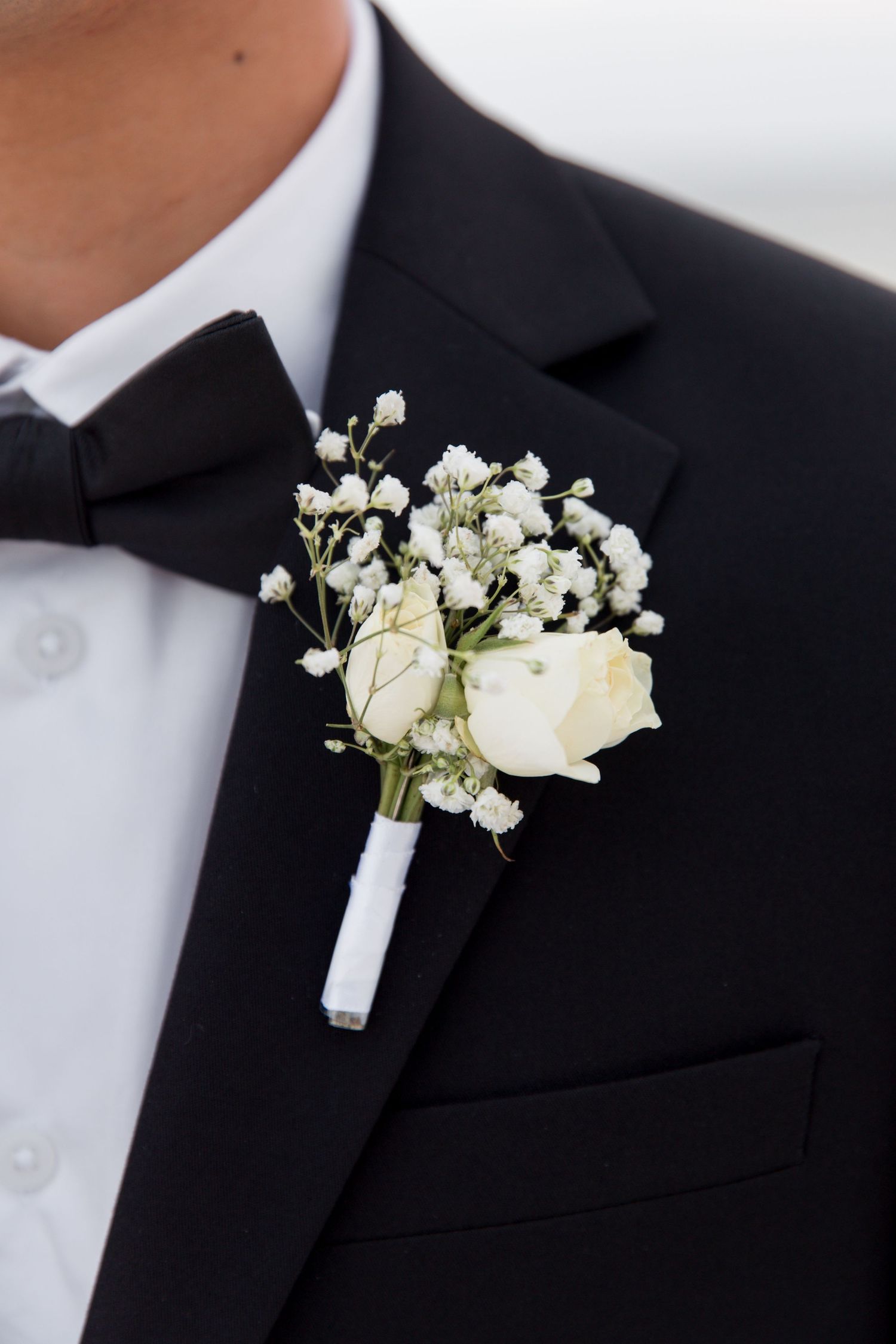 Classic white rose and baby's breath boutonniere on groom's black tuxedo lapel.