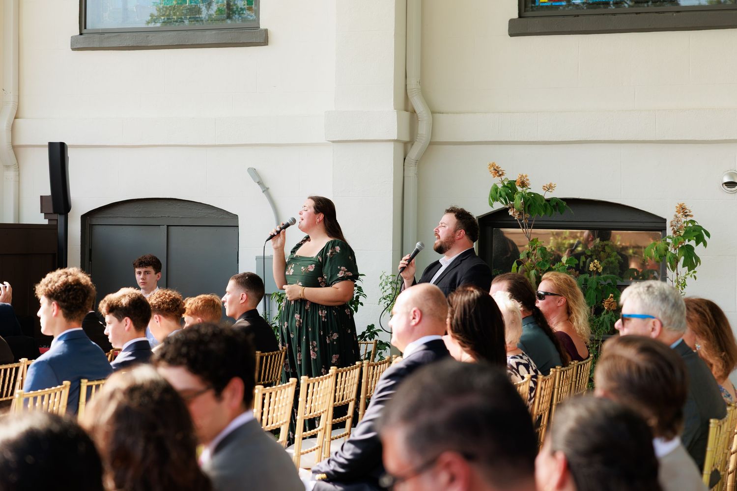 Two singers performing at a microphone during an elegant indoor wedding reception with seated guests.