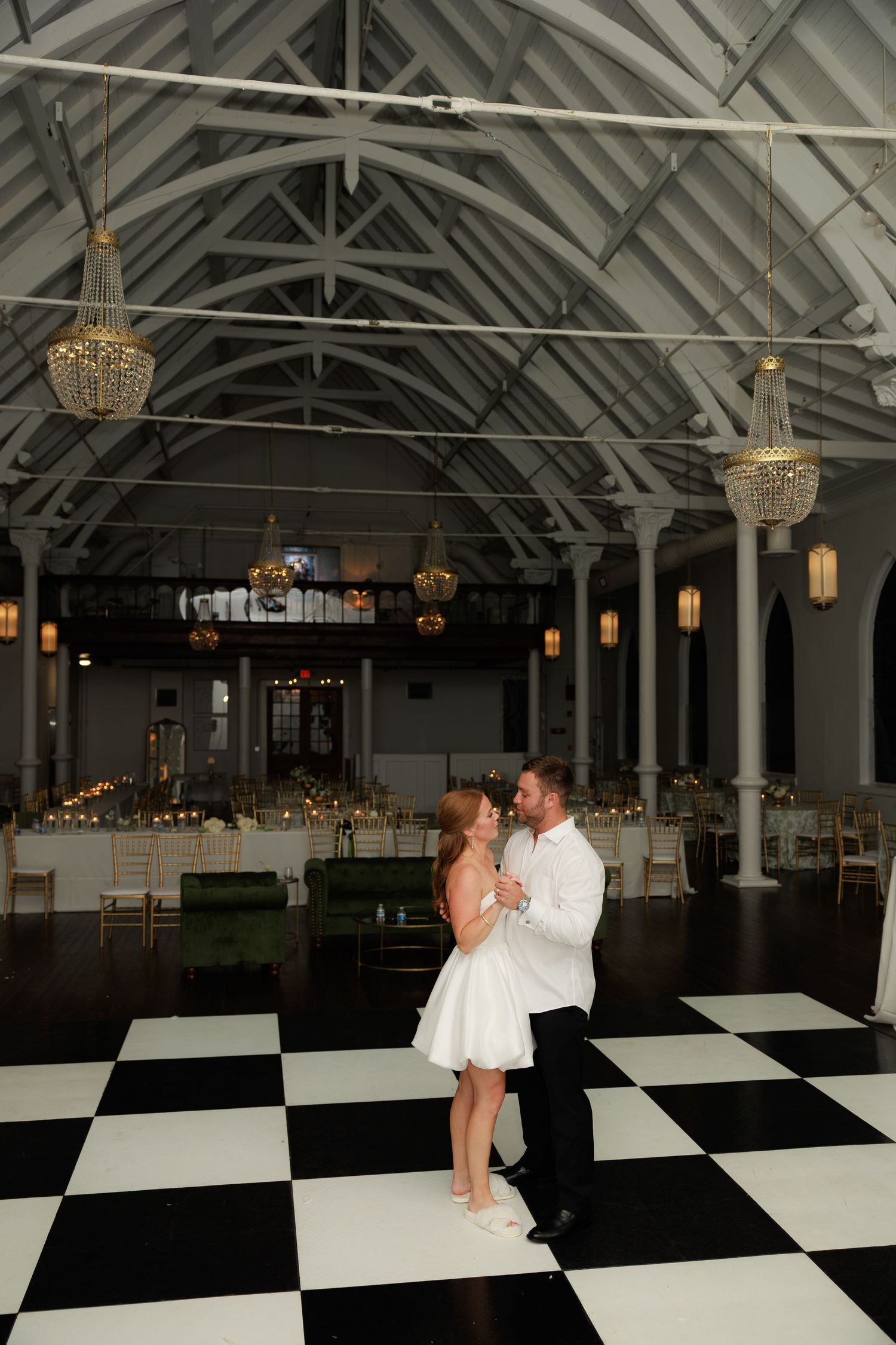 Bride and groom sharing first dance on black and white checkered floor in elegant venue.