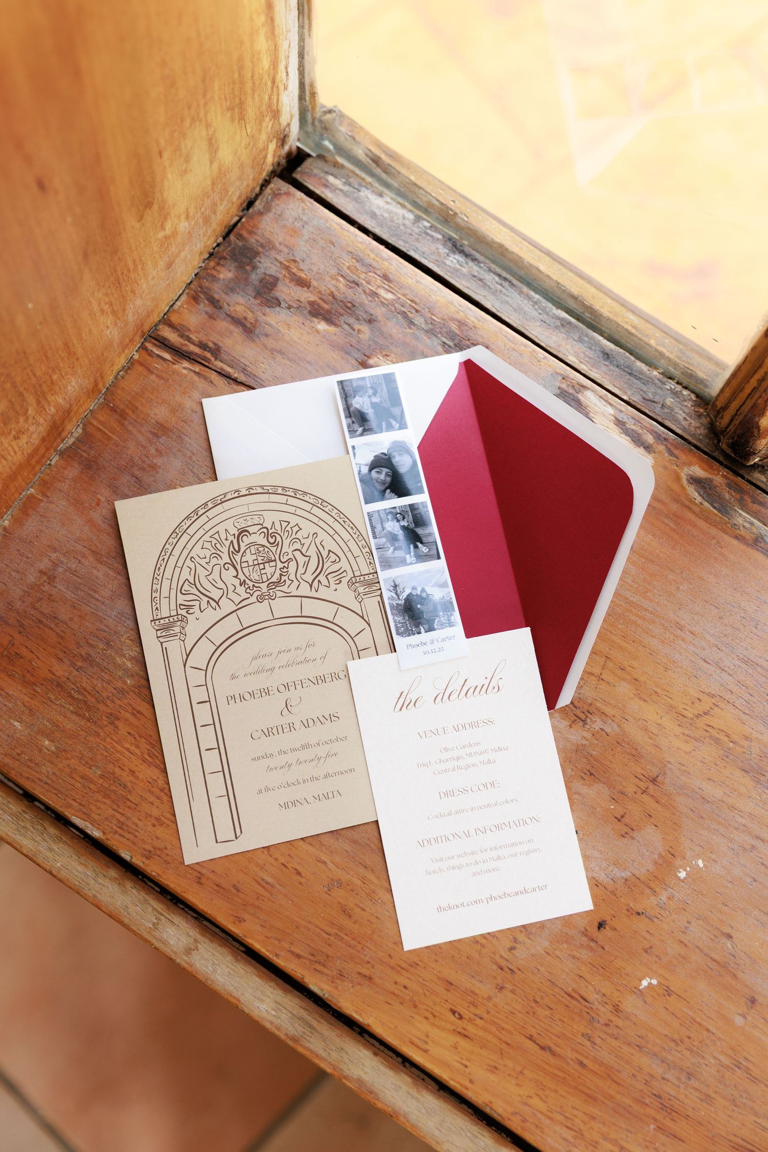 Wedding invitation suite with ornate arch design and red envelope displayed on rustic wooden surface.