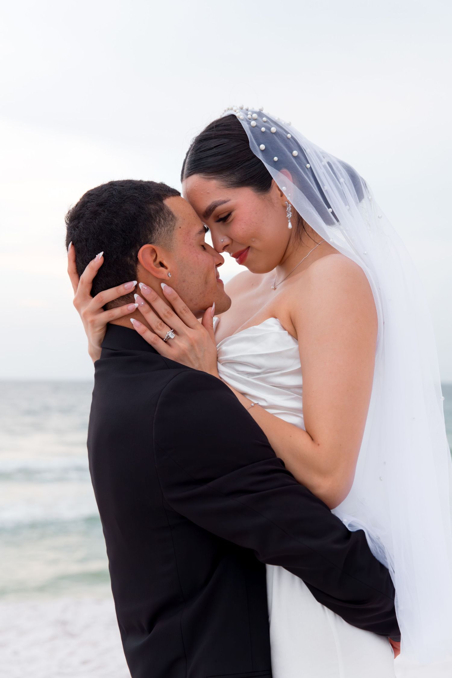 Bride and groom share tender moment during beach wedding photoshoot.