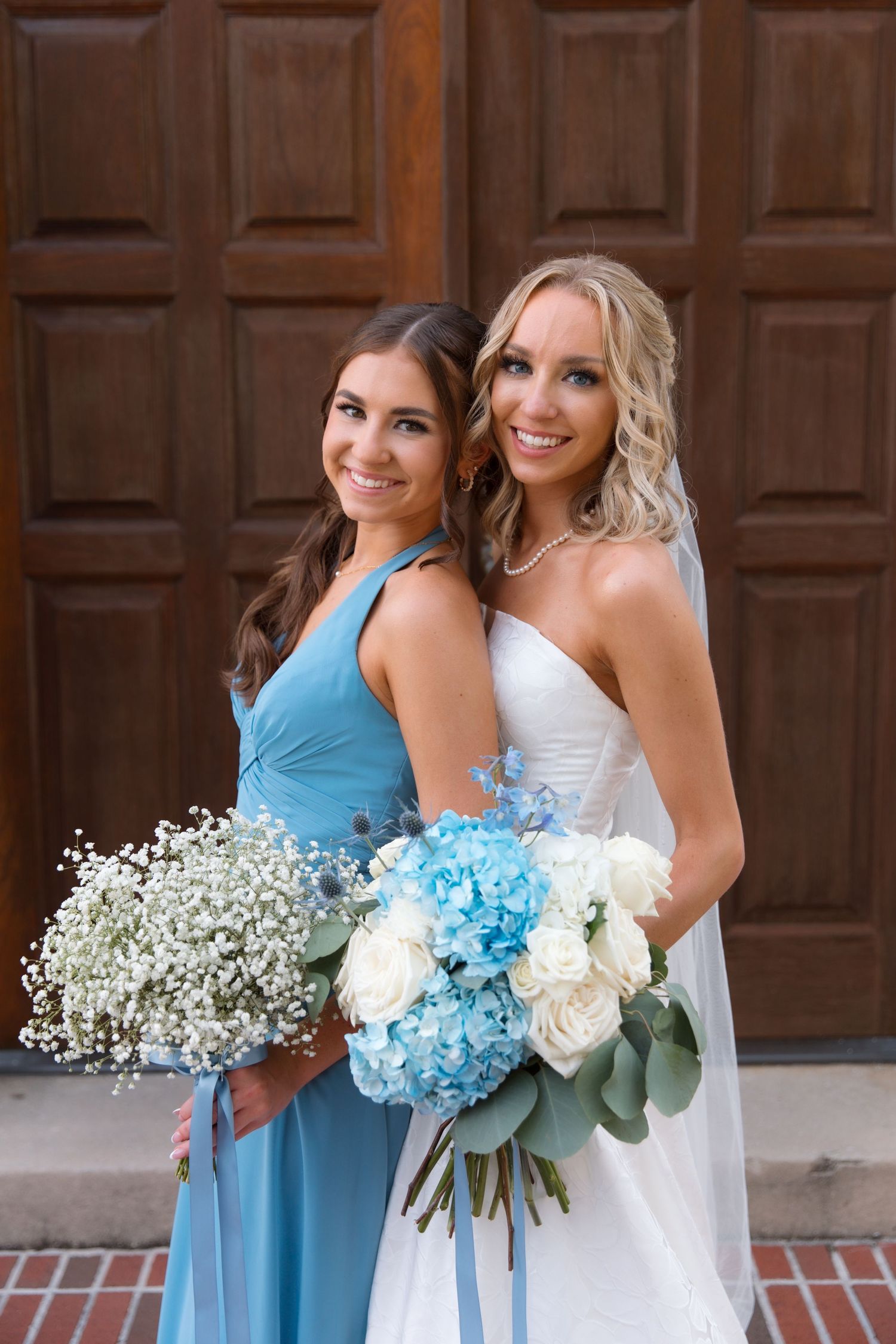 Two people in blue bridesmaid dress and white wedding gown holding blue and white bouquets.