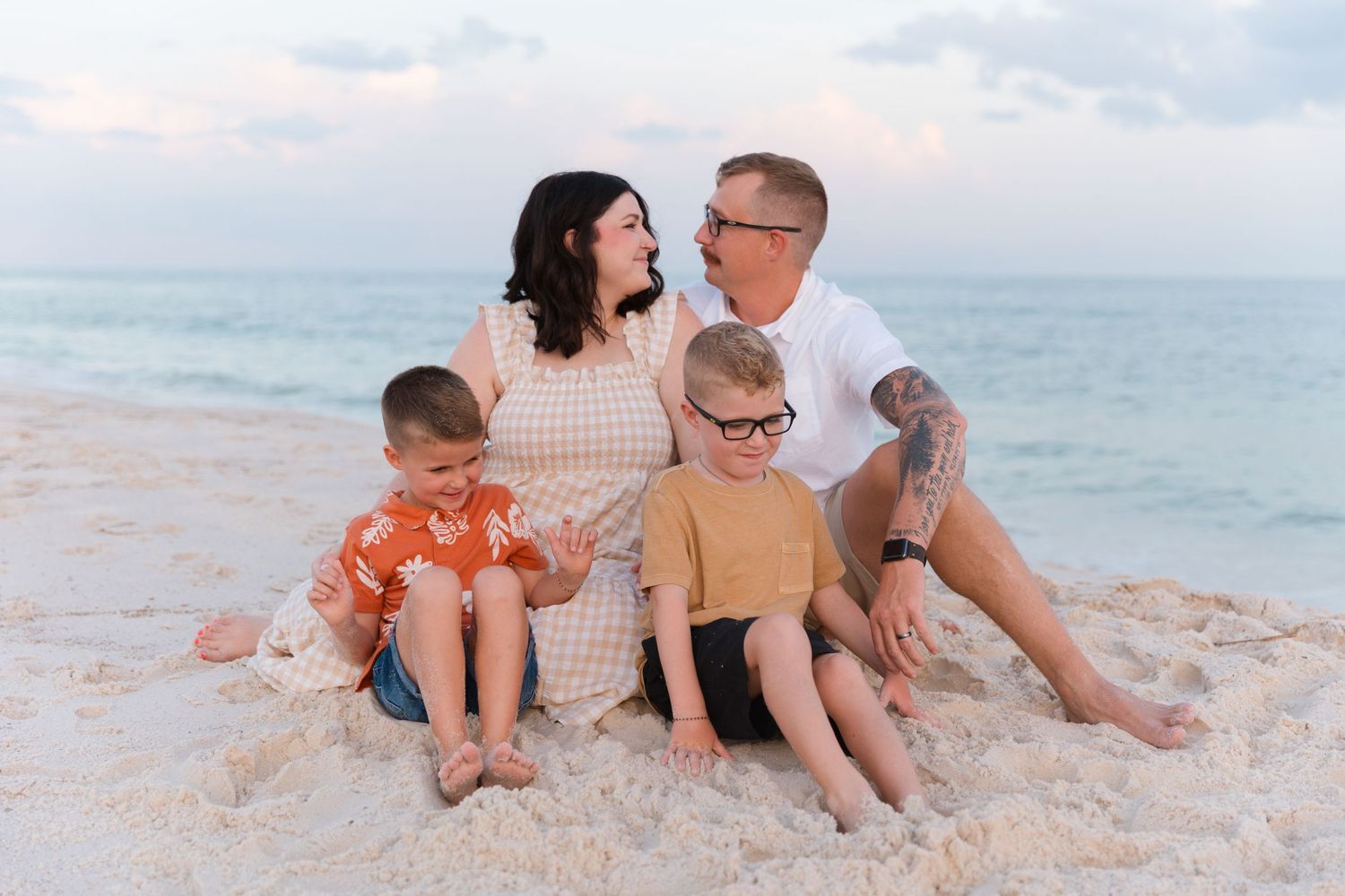 Family sitting together on sandy beach with ocean waves in background.