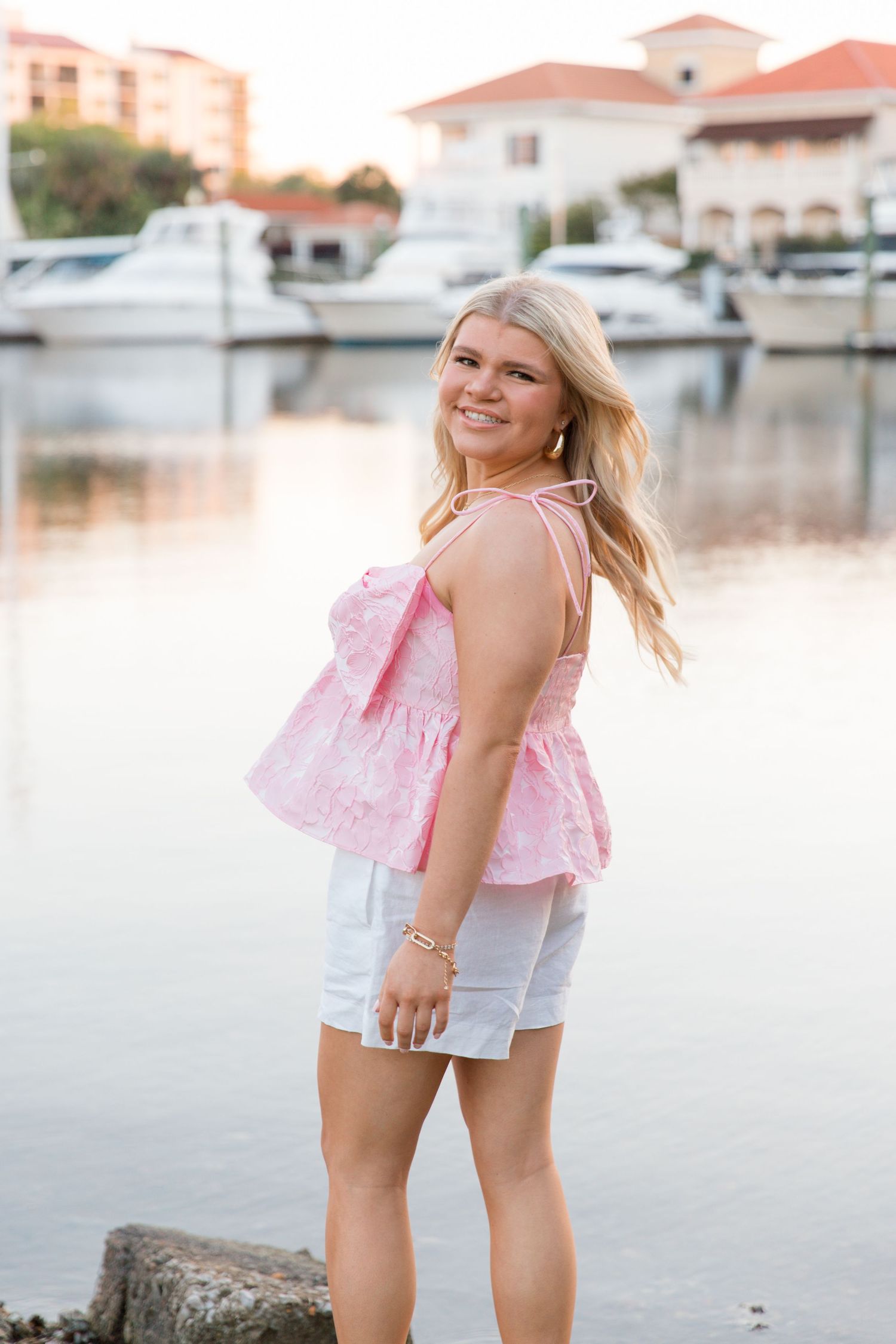 A series of outdoor portraits showing a person in a pink top and white shorts posing near a marina at sunset.