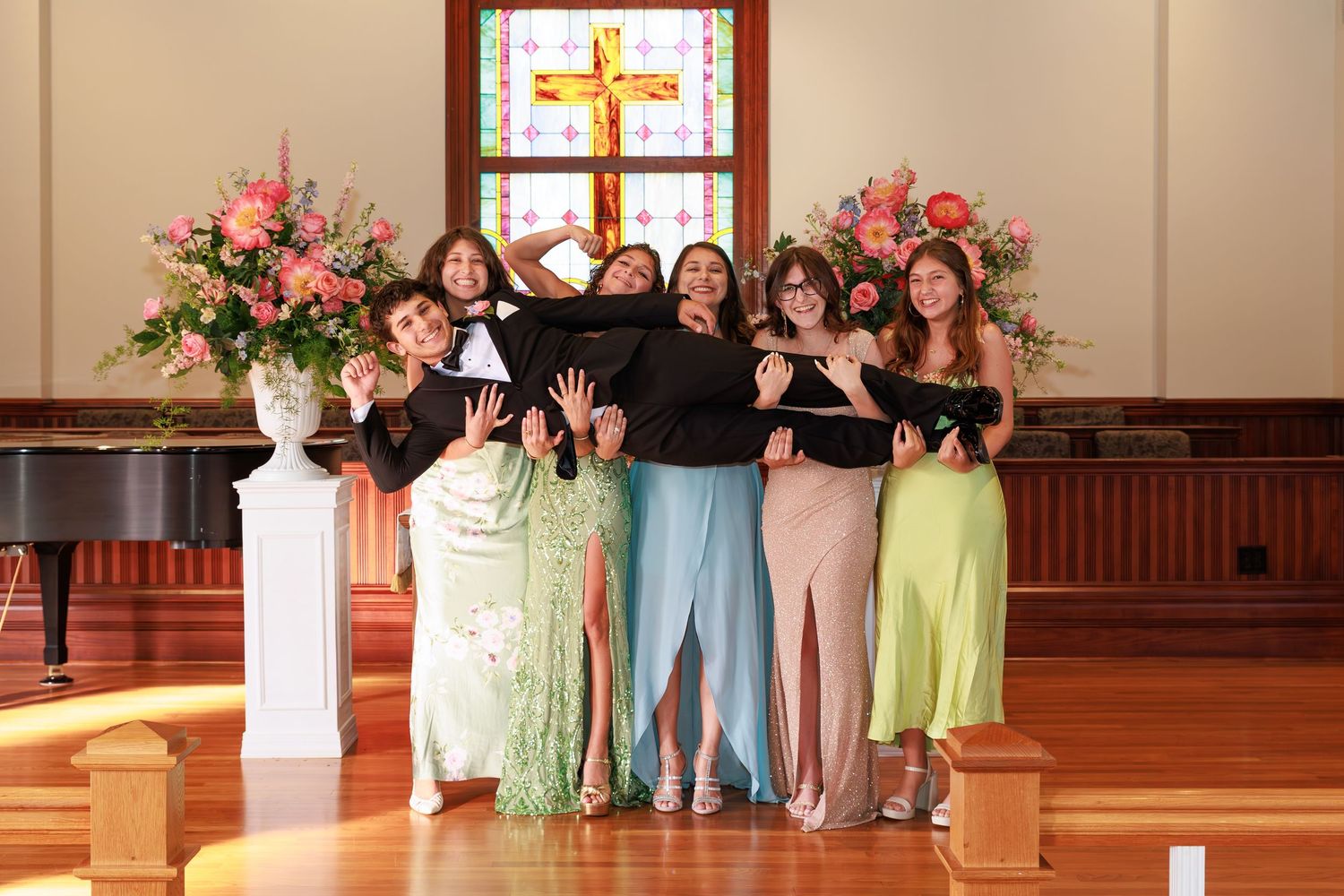 A row of people in pastel-colored formal attire stand together in a church sanctuary for a celebration.