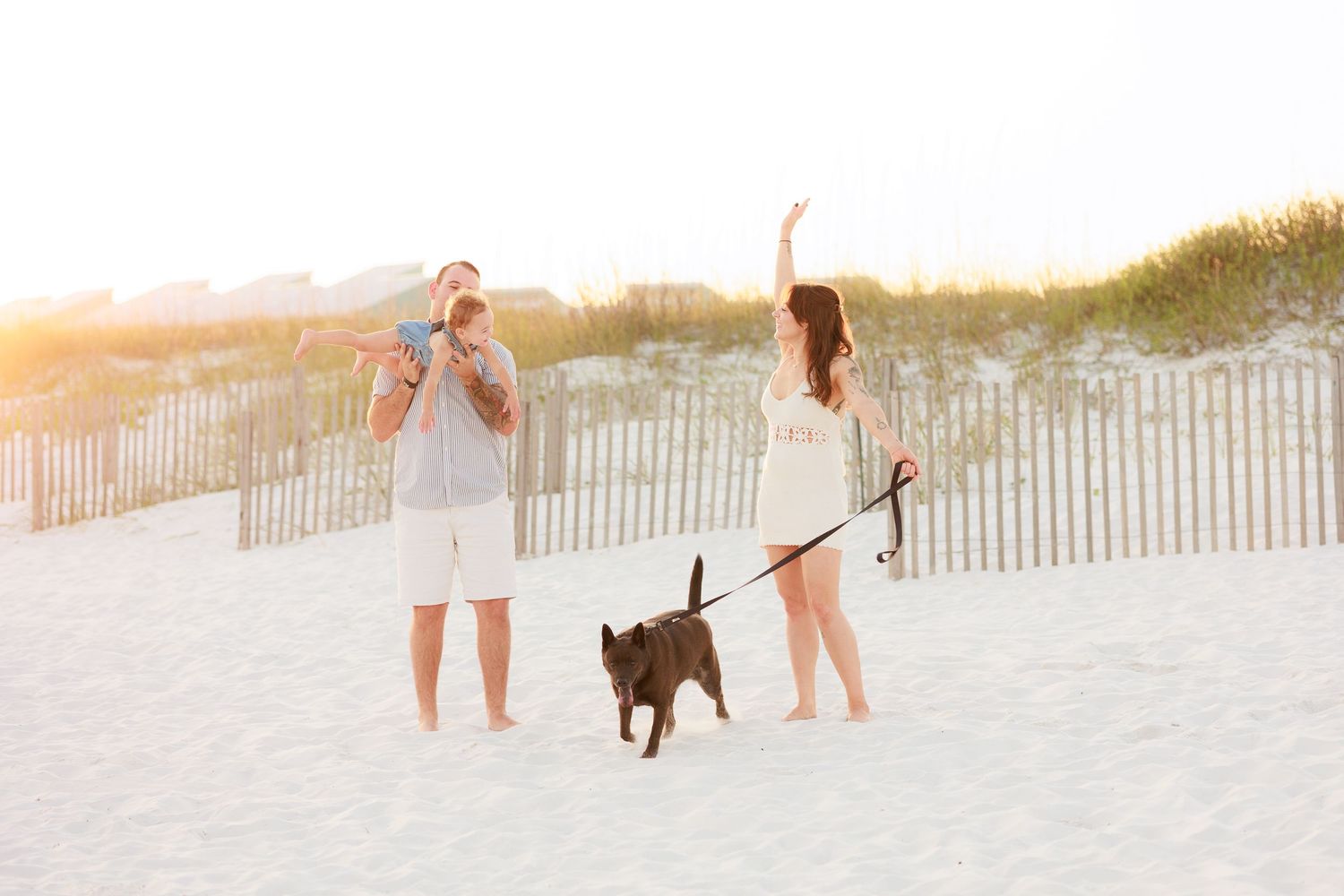 Family with baby and dog enjoying golden hour on a white sand beach.