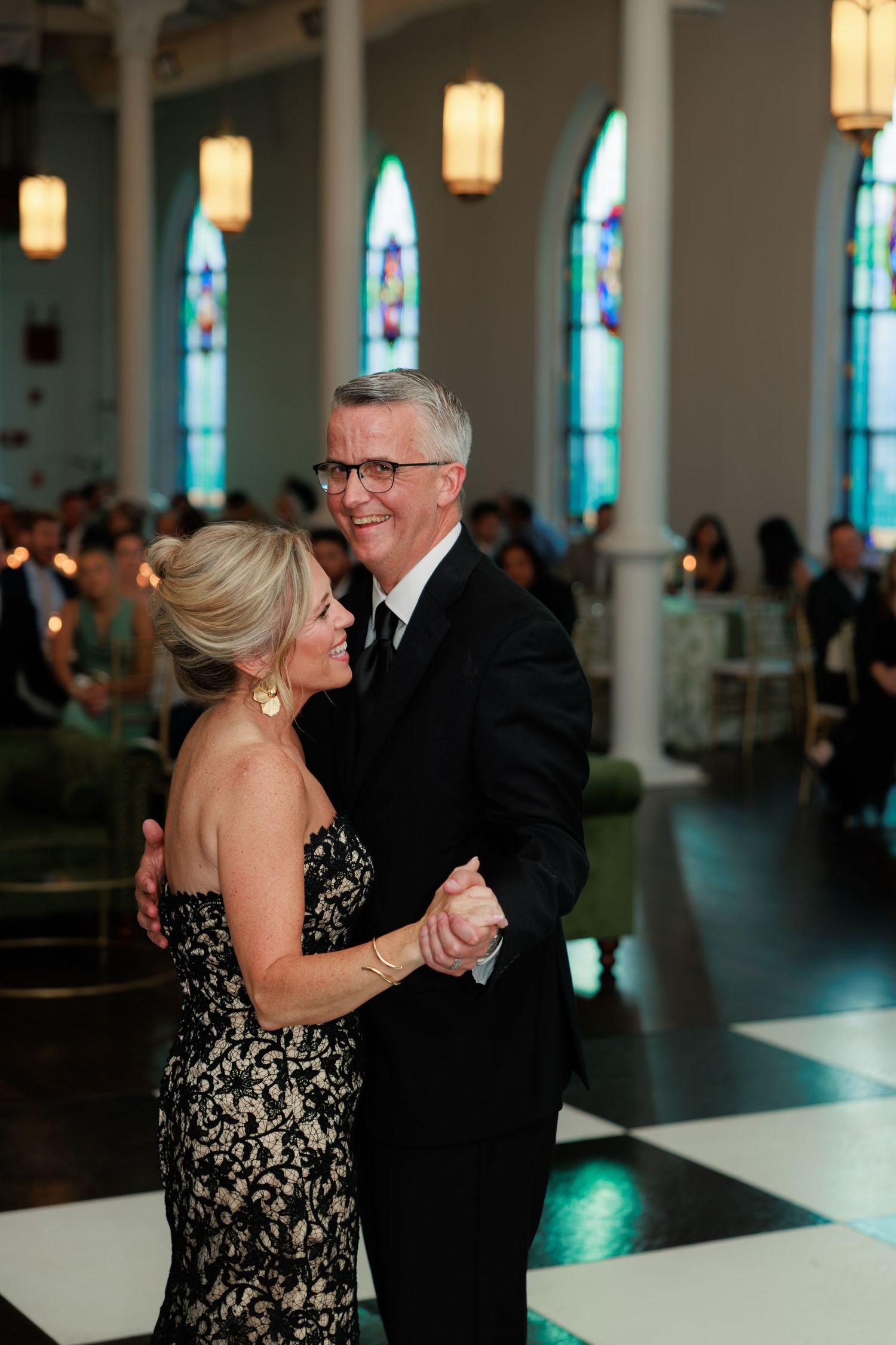 Couple dancing elegantly at a wedding reception in a beautifully lit church with stained glass windows.