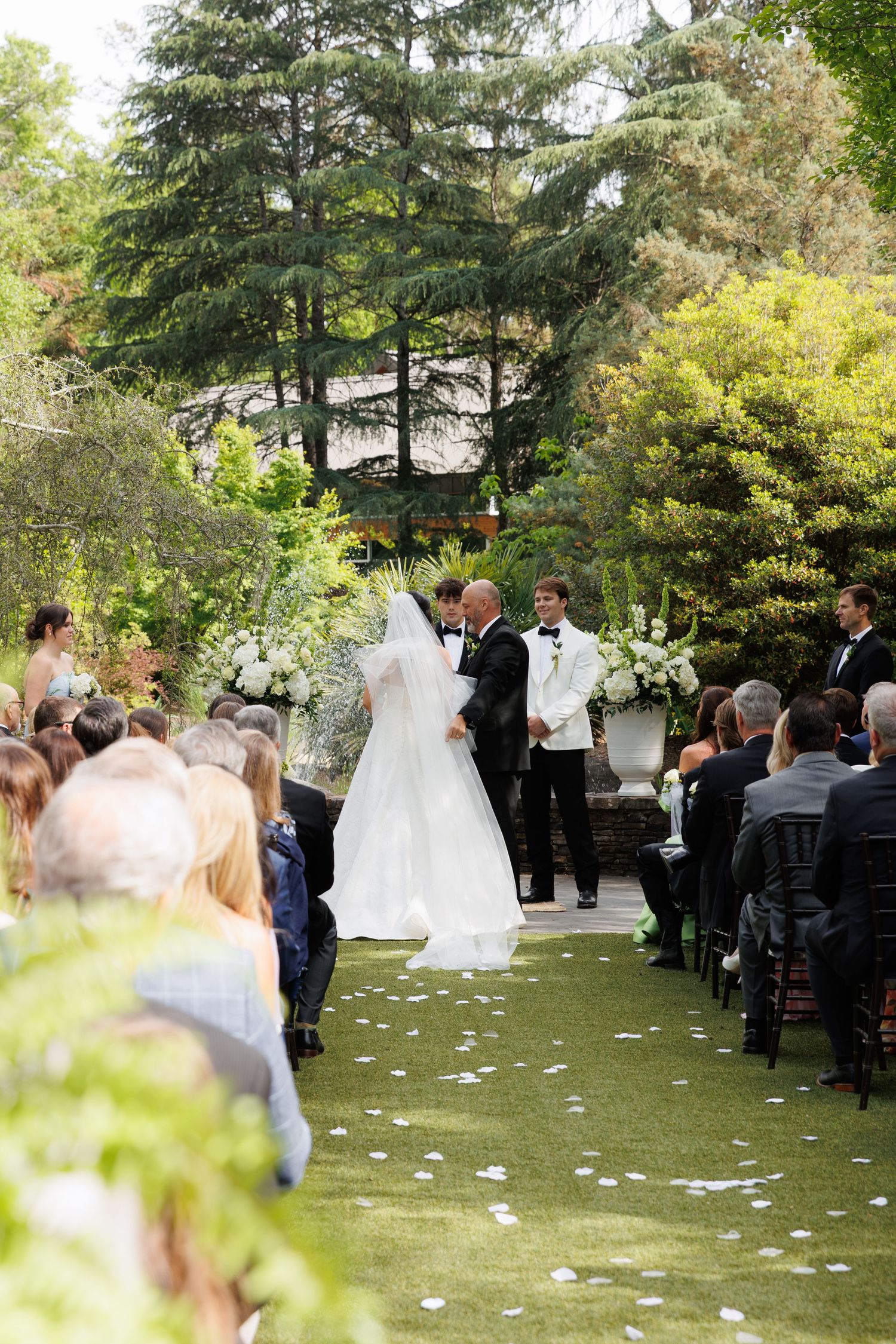 Bride and groom exchange vows at romantic outdoor garden wedding ceremony with white floral arrangements.